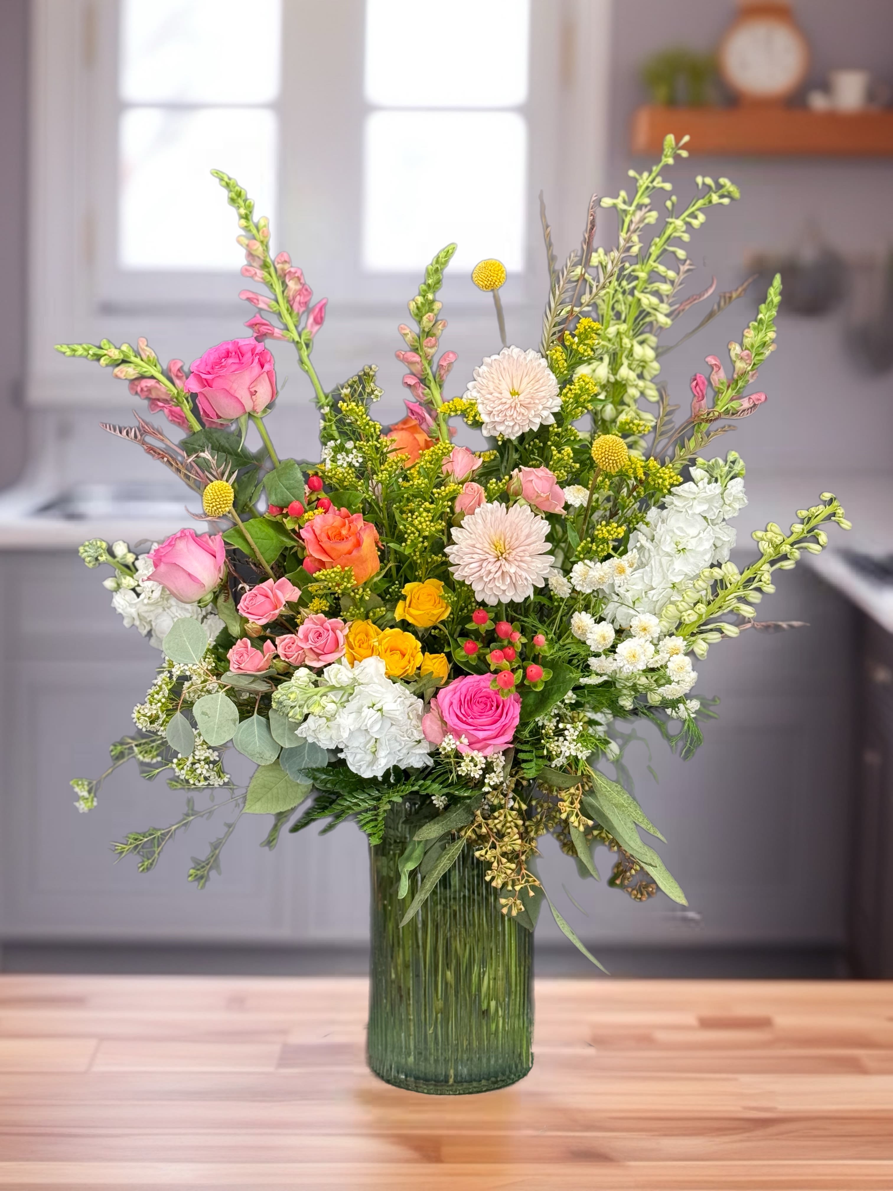 Mixed pink, white, and yellow flowers in a tall green glass vase