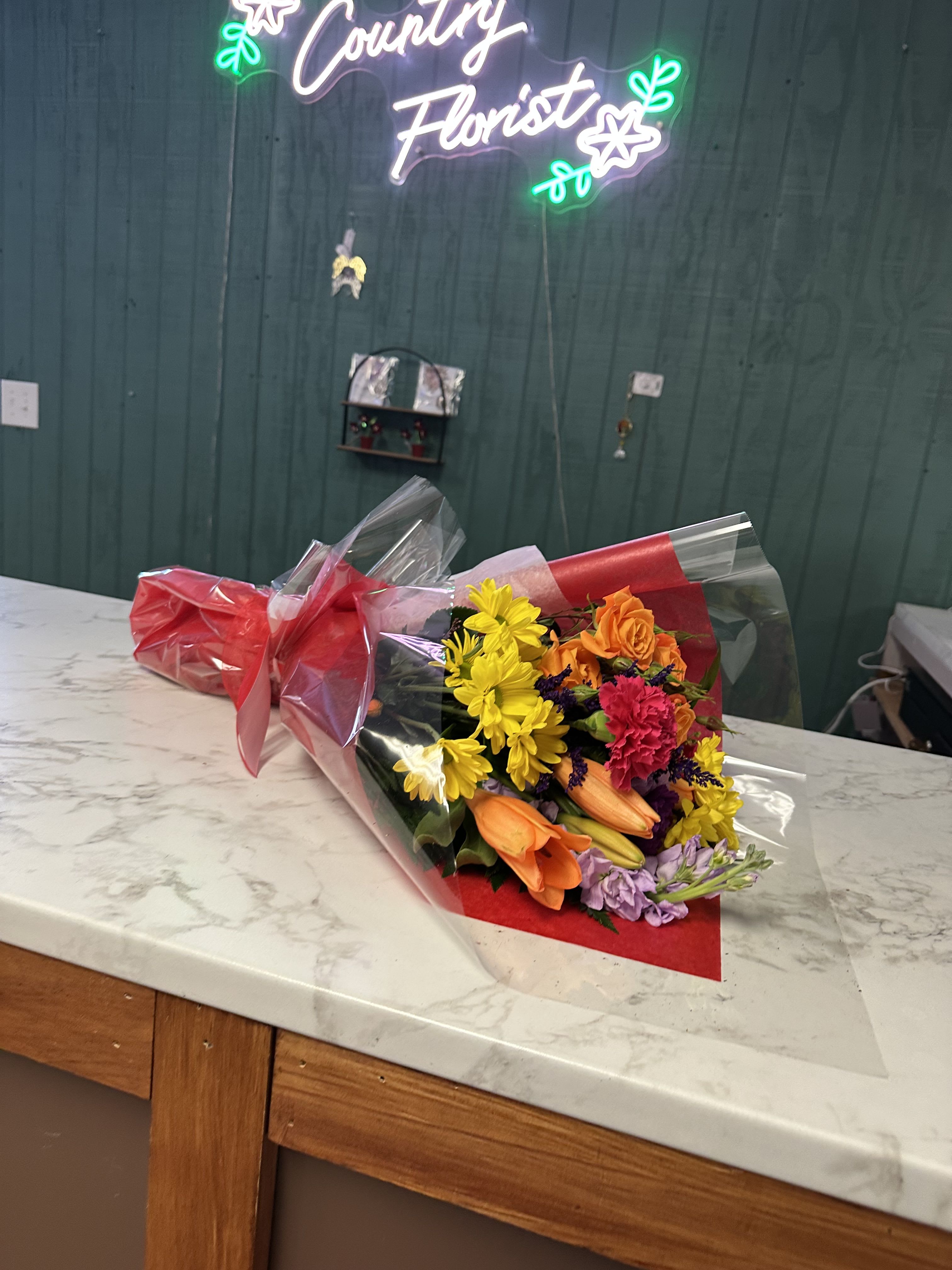 Wrapped bouquet with yellow daisies, orange roses, and pink carnations