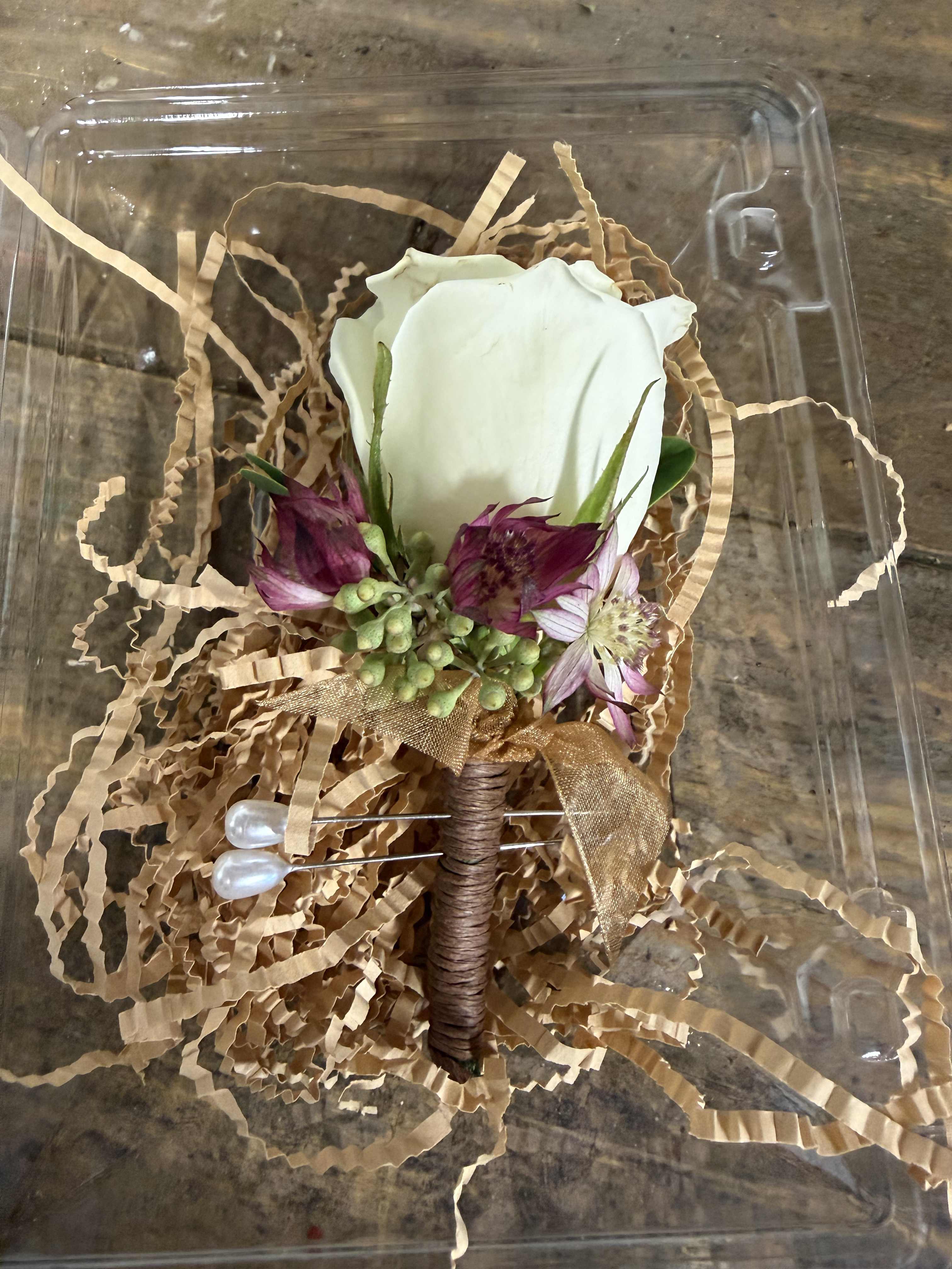 White rose boutonniere with purple flowers in a clear plastic box