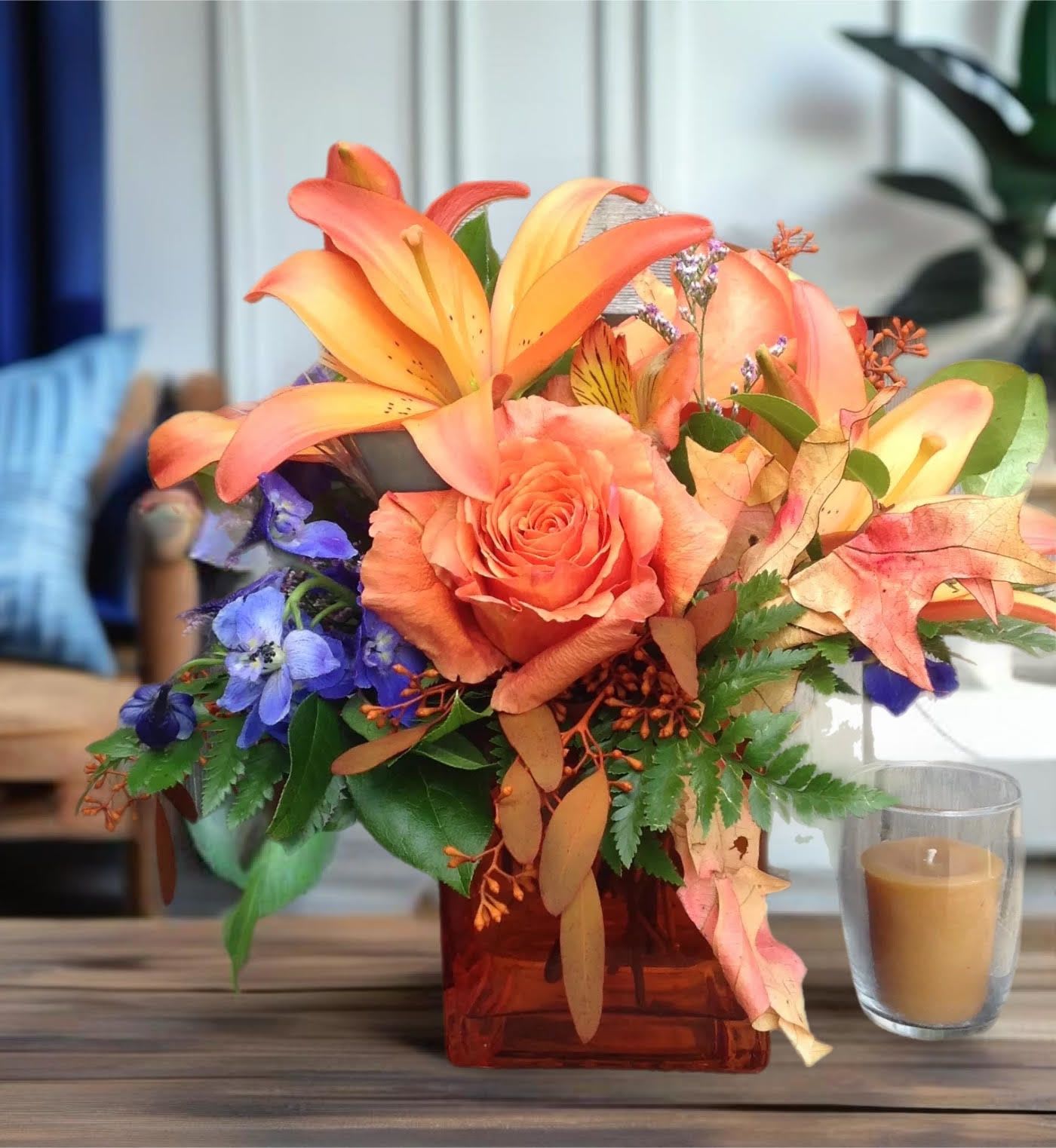 Orange Spice Cube - Subtle with a flicker of fire, this stunning floral arrangement is perfect for someone who loves life. A stylish orange glass cube vase, filled with Asiatic lilies, roses,  accented with autumn leaves.     