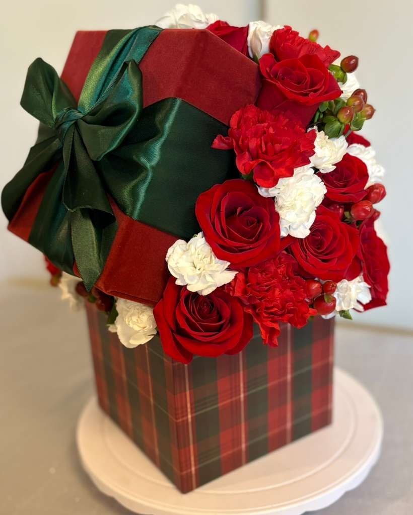 Christmas in a Box - Celebrate the magic of the season with this luxurious floral design  a perfect blend of classic holiday colors and timeless elegance.  Featuring vibrant red roses, scarlet carnations, and soft white blooms, delicately accented with festive berries. The arrangement is presented in a plaid holiday box wrapped with a deep green satin bow, evoking the warmth and nostalgia of Christmas.   Ideal as a holiday gift, a centerpiece for festive dinners, or a special touch of joy for any space. Each piece is handcrafted with love and attention to detail, bringing the spirit of Christmas into every petal.   Exclusively by Blum Moon Flowers