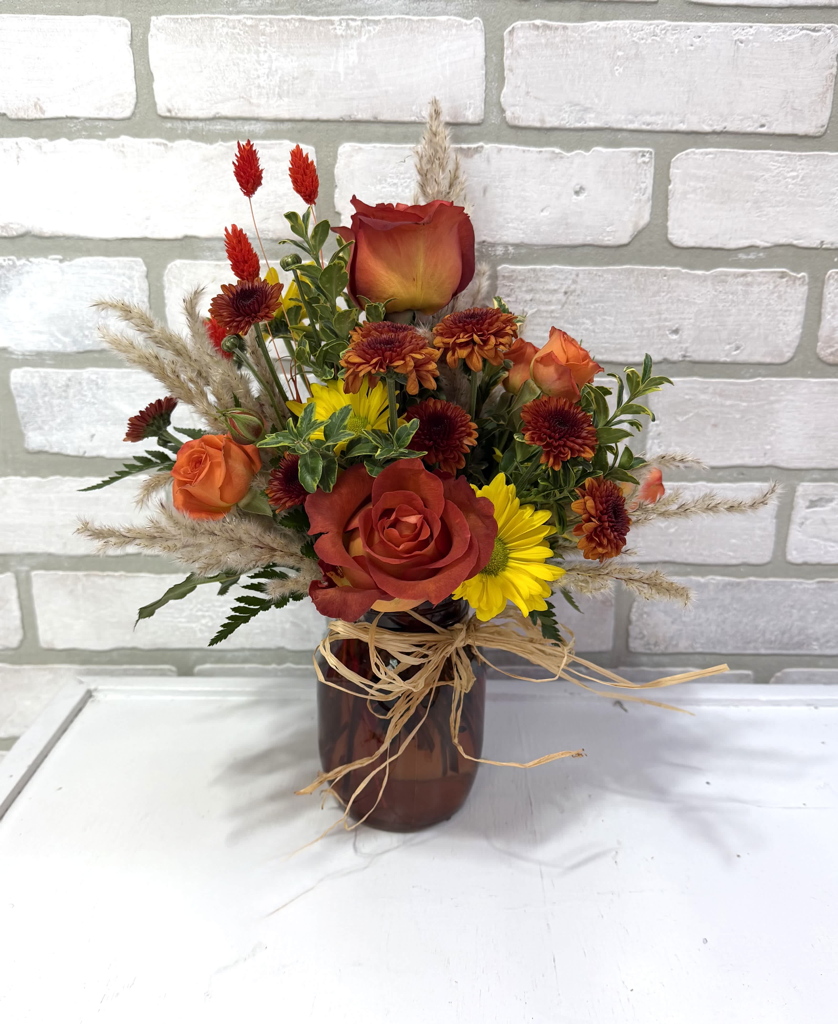 Mixed bouquet of red and orange roses with yellow daisies in a brown vase