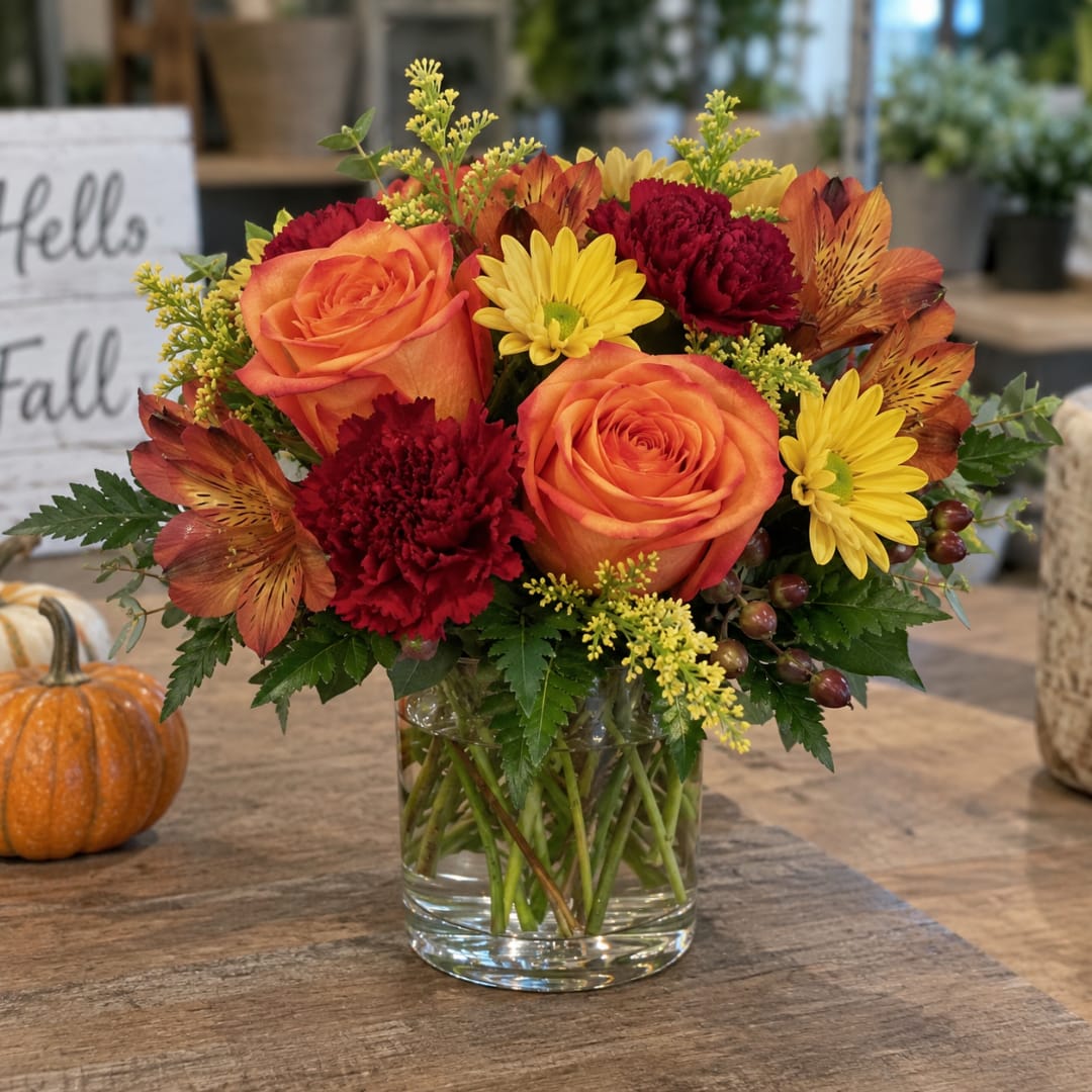 Orange roses and fall flowers arranged in a clear glass vase