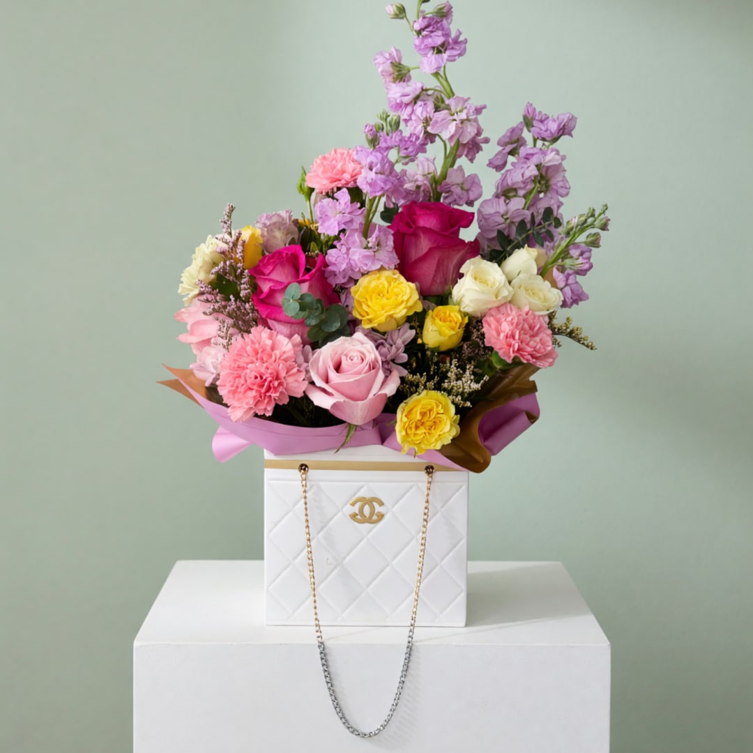 Mixed bouquet of pink, yellow, and lavender flowers in a white box