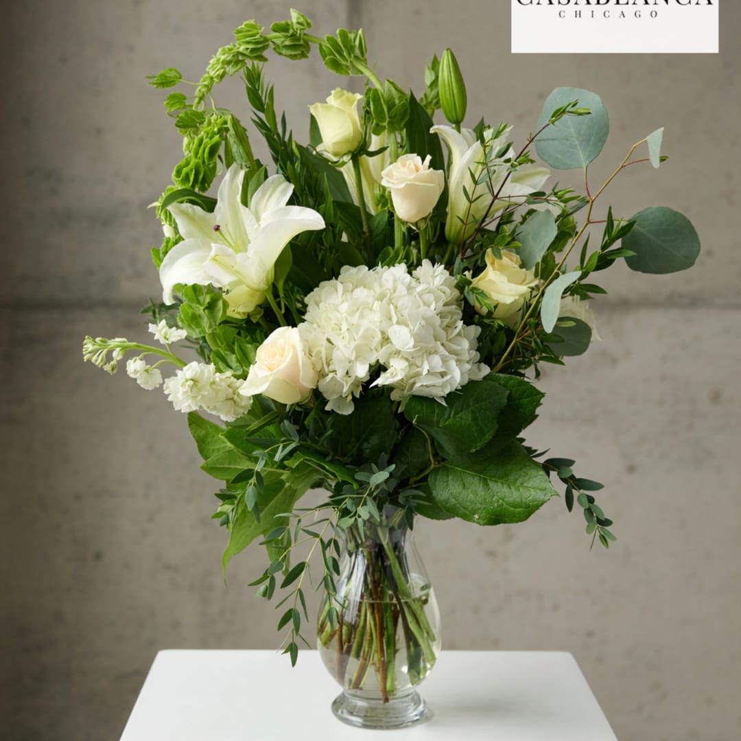 White lilies and roses in a clear glass vase with greenery