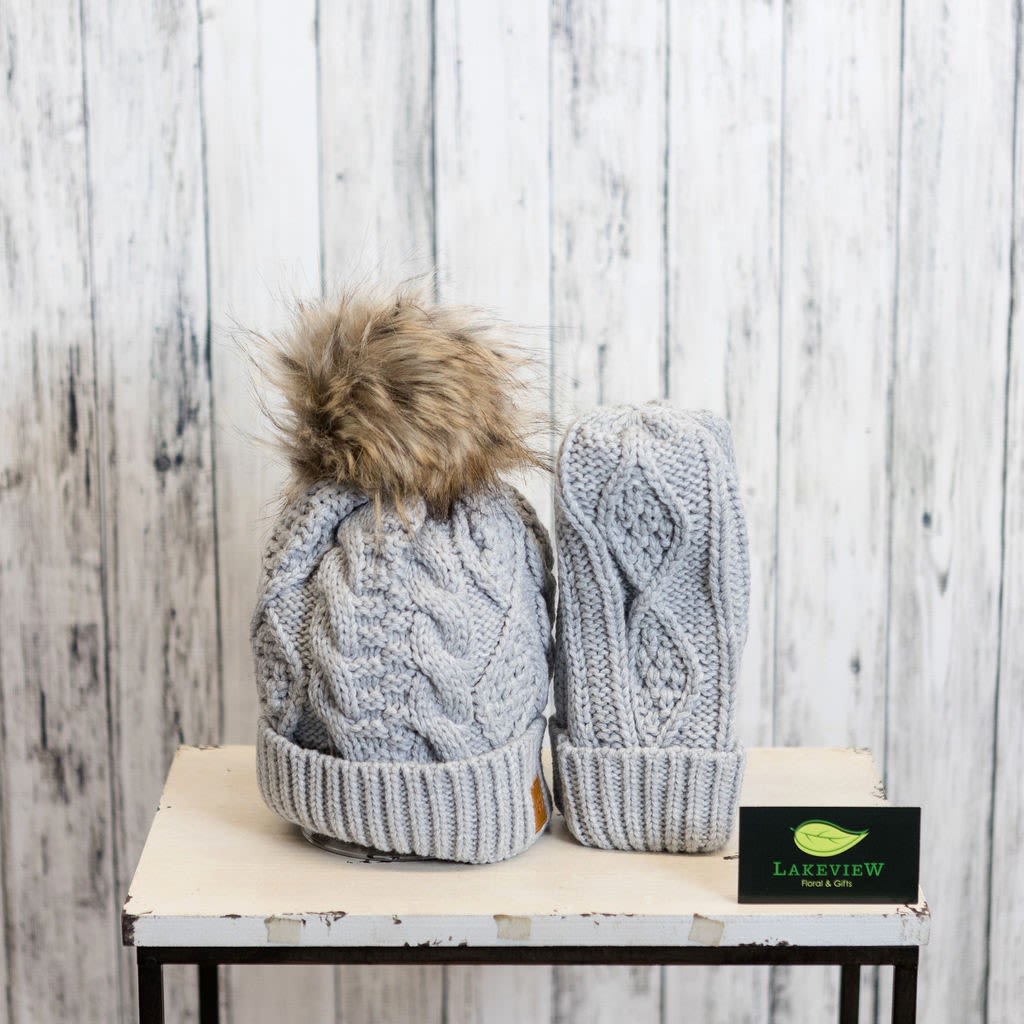 Two gray knit winter hats with faux fur pom-poms on a table