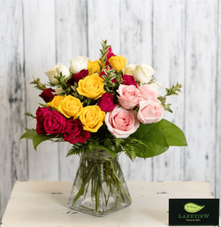 Mixed bouquet of red, yellow, white, and pink roses in a clear glass vase