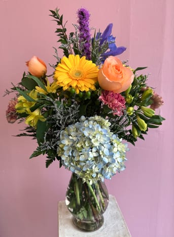 Mixed bouquet in a glass vase with yellow, peach, blue, and purple flowers