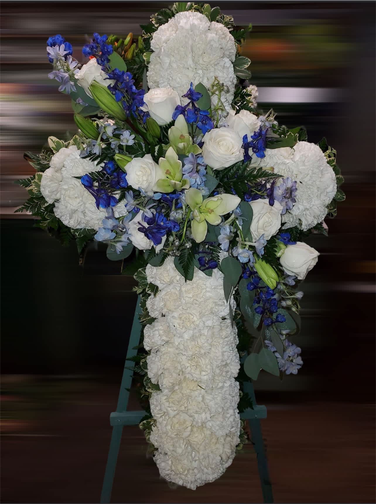 White floral cross on an easel with blue and green accents