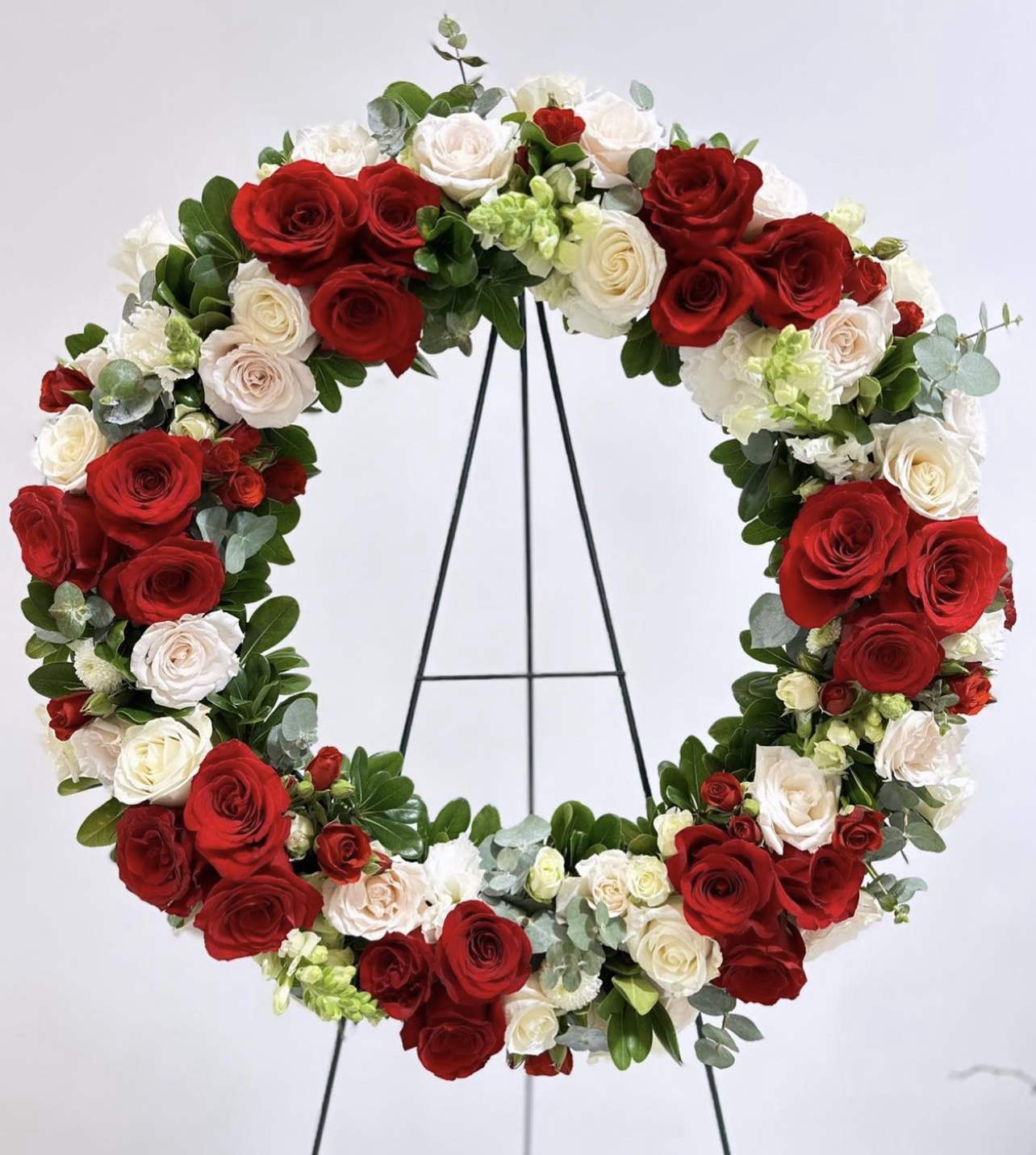 Circular wreath of red and white roses on a black stand