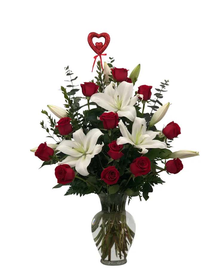 Red roses and white lilies in a clear glass vase with a heart pick