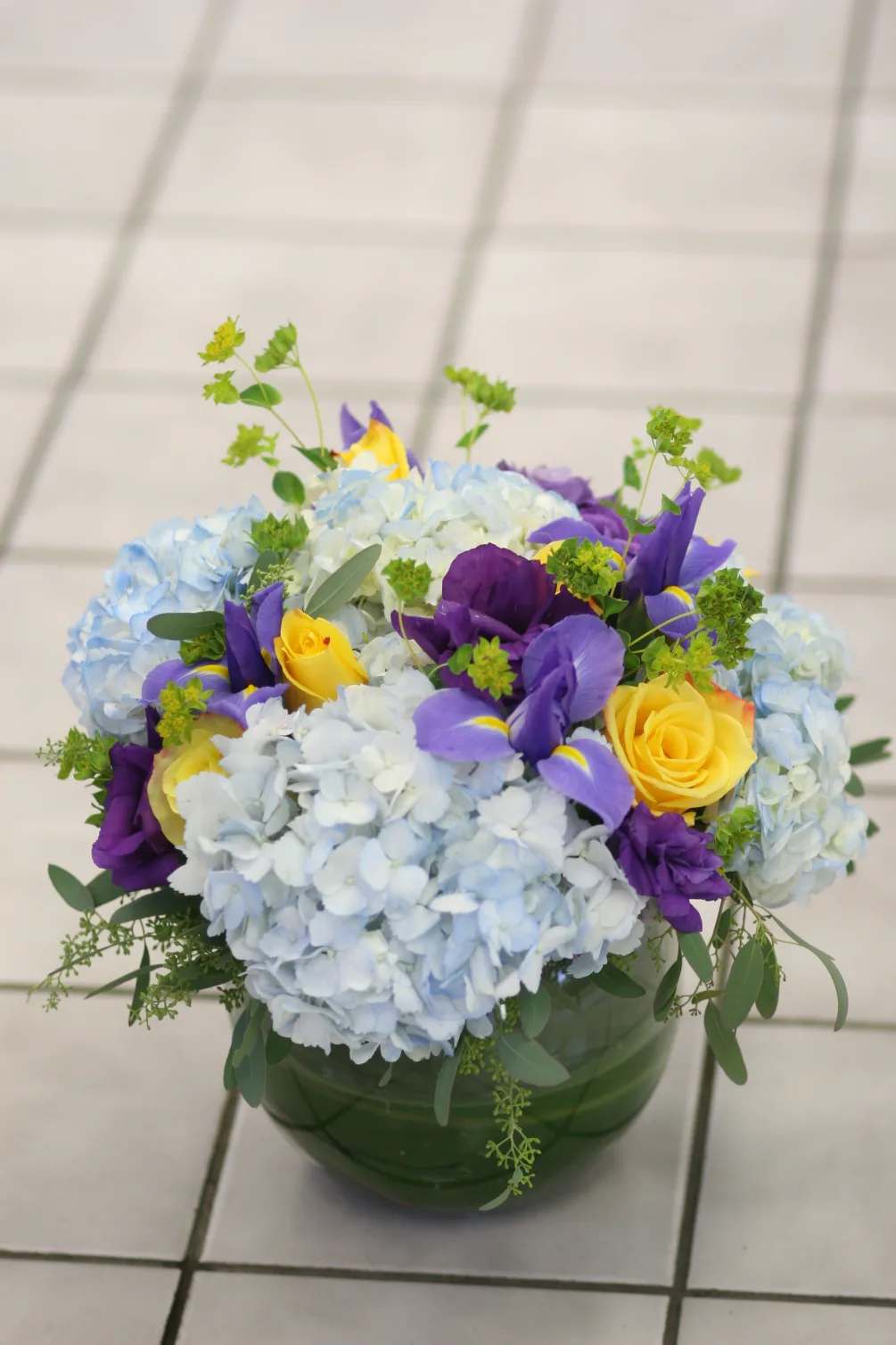 Blue hydrangeas with yellow and purple roses in a green vase