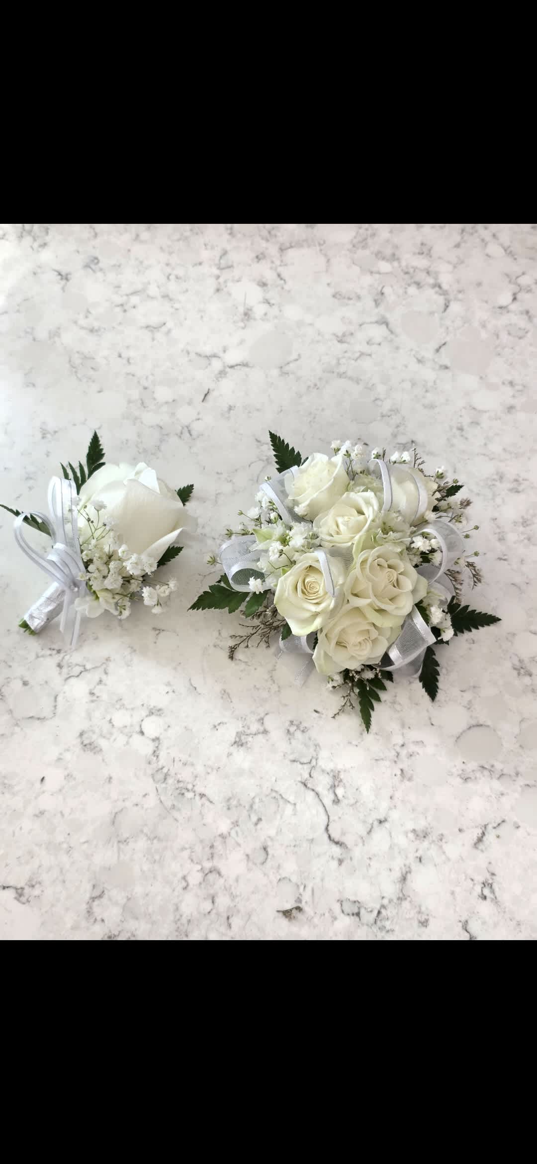 Boutonniere - White Rose - A single white rose boutonniere that reads as timeless and quietly elegant-the perfect finishing touch for a groom, groomsman, or father of the bride on wedding day. This wedding boutonniere pairs a crisp white rose with delicate green sprigs and a soft pink accent, pinned to a suit jacket for a clean, traditional look that still feels thoughtfully modern. It's designed to make the person you're honoring feel composed and cherished in the moment.  Crafted to sit neatly on a lapel, the boutonniere uses fresh roses and tasteful greenery arranged for a low-profile silhouette that complements gray, navy, or black suits and a variety of ties. The white and green palette keeps the piece versatile for classic, garden, or formal ceremonies, while the pale pink detail adds a gentle warmth that photographs beautifully in close-up shots. The set includes the boutonniere and pin for secure attachment to the suit jacket.  Ideal for weddings, anniversaries, or any formal celebration where attention to detail matters-this boutonniere sends the message that the wearer is honored and part of the moment. For local delivery in National City, CA, or pickup, order with your wedding date to ensure fresh blooms; keep the boutonniere cool and dry until it's pinned for lasting freshness.