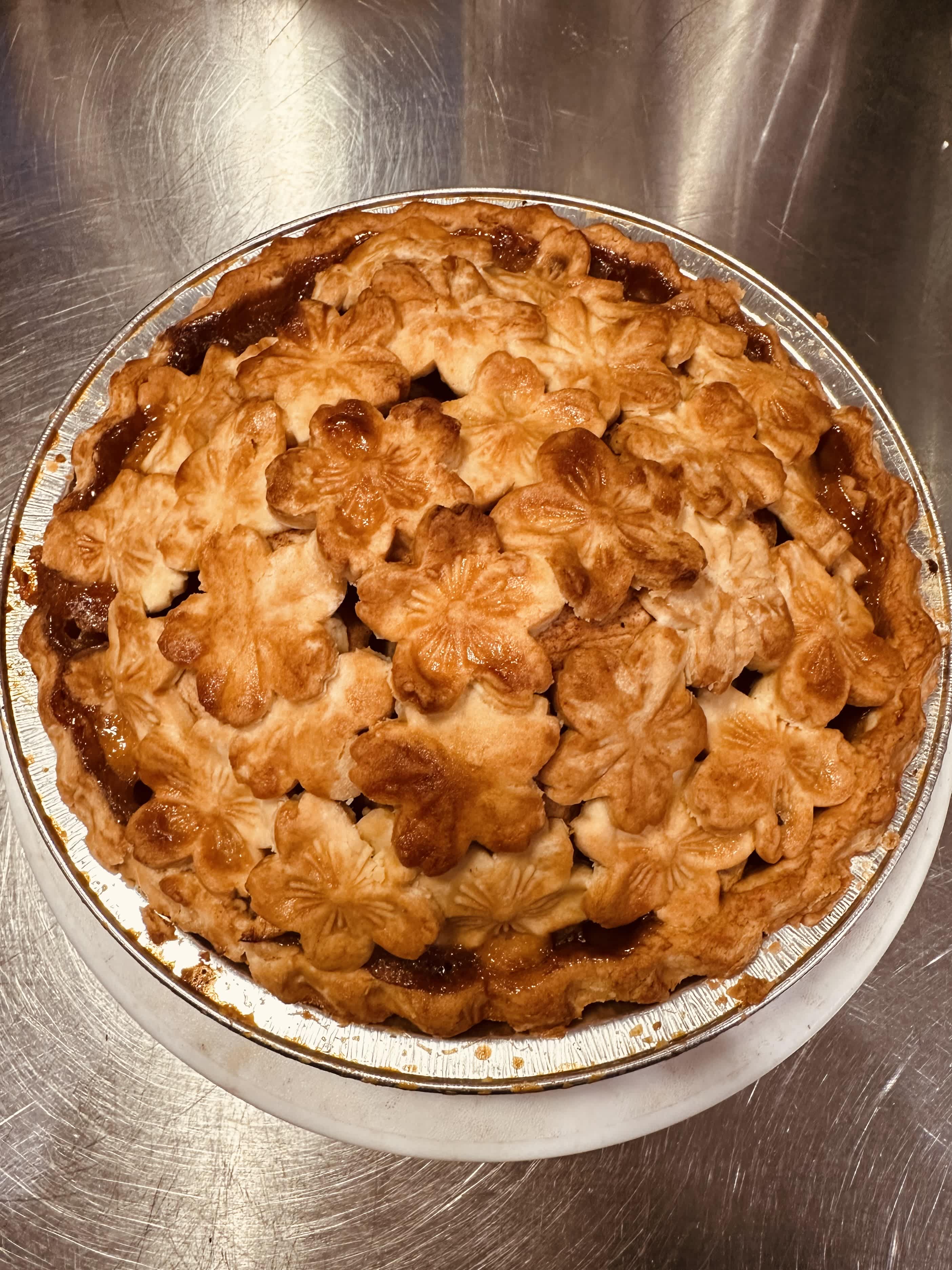 A baked pie with a decorative flower-shaped crust in a foil pan