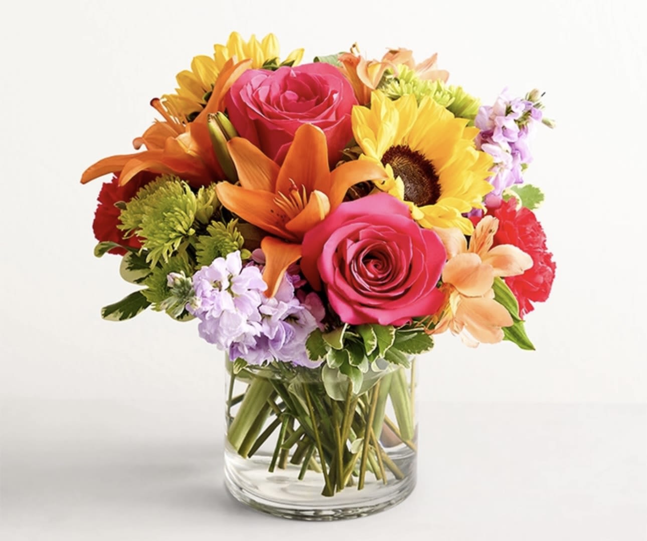 Mixed bouquet of roses, lilies, and sunflowers in a clear glass vase