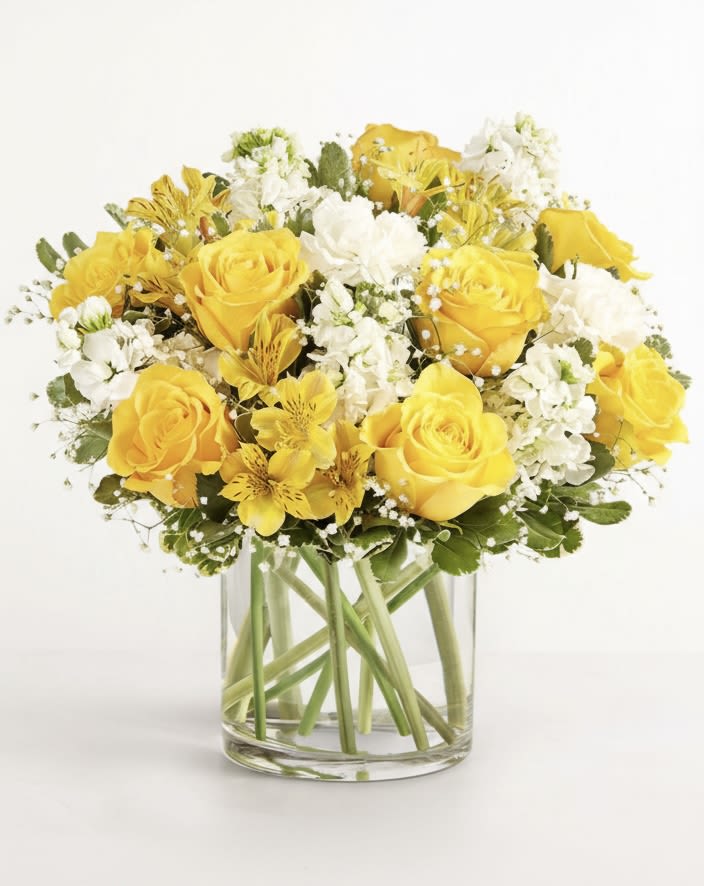 Yellow roses and white flowers arranged in a clear glass vase