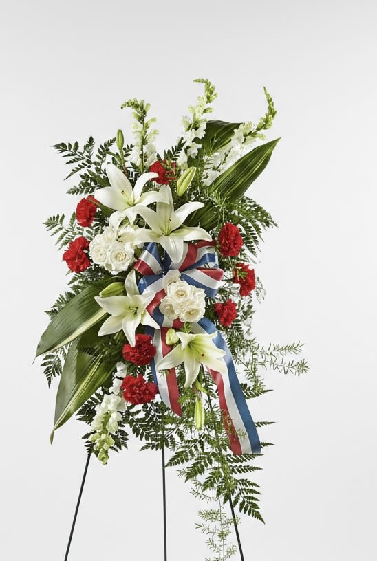 Standing floral spray with white lilies, red carnations, and a red-white-blue ribbon