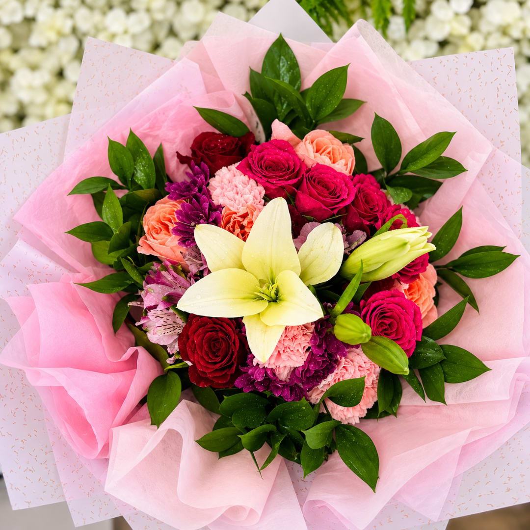 Pink bouquet with roses, carnations, and a white lily wrapped in pink paper