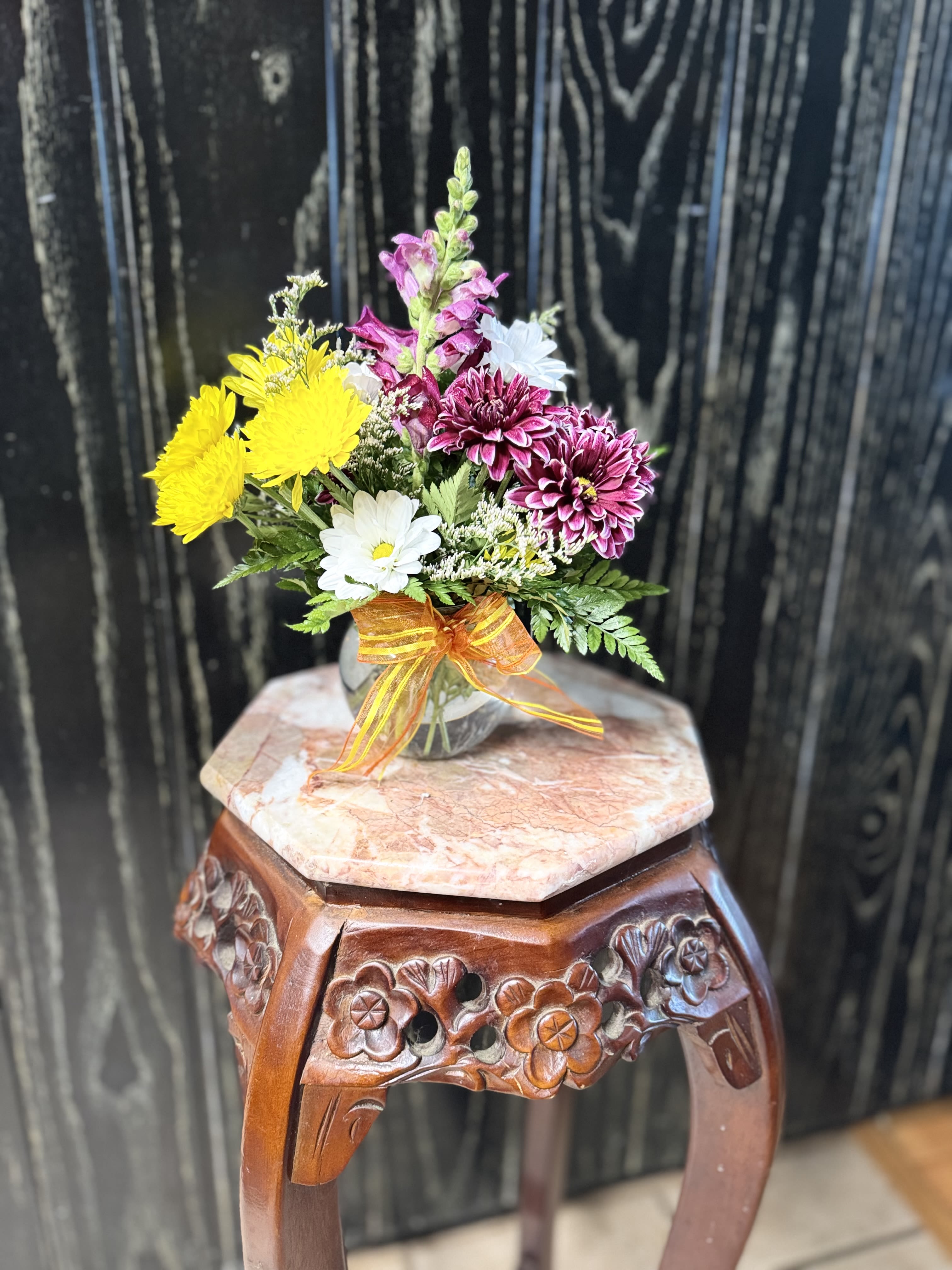 Small mixed flower bouquet in a clear glass vase with an orange ribbon