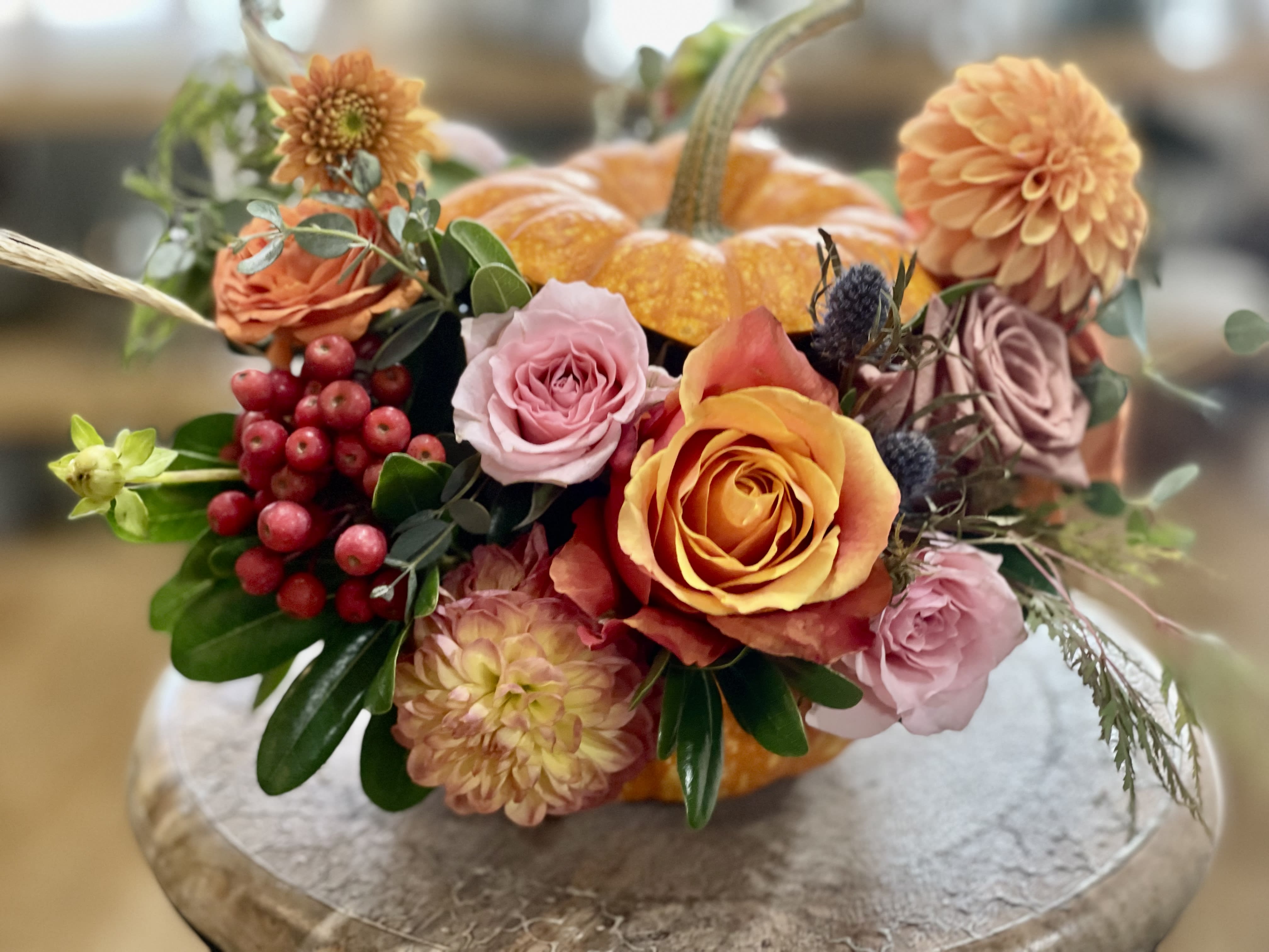 Autumn floral arrangement with roses and dahlias around a small pumpkin