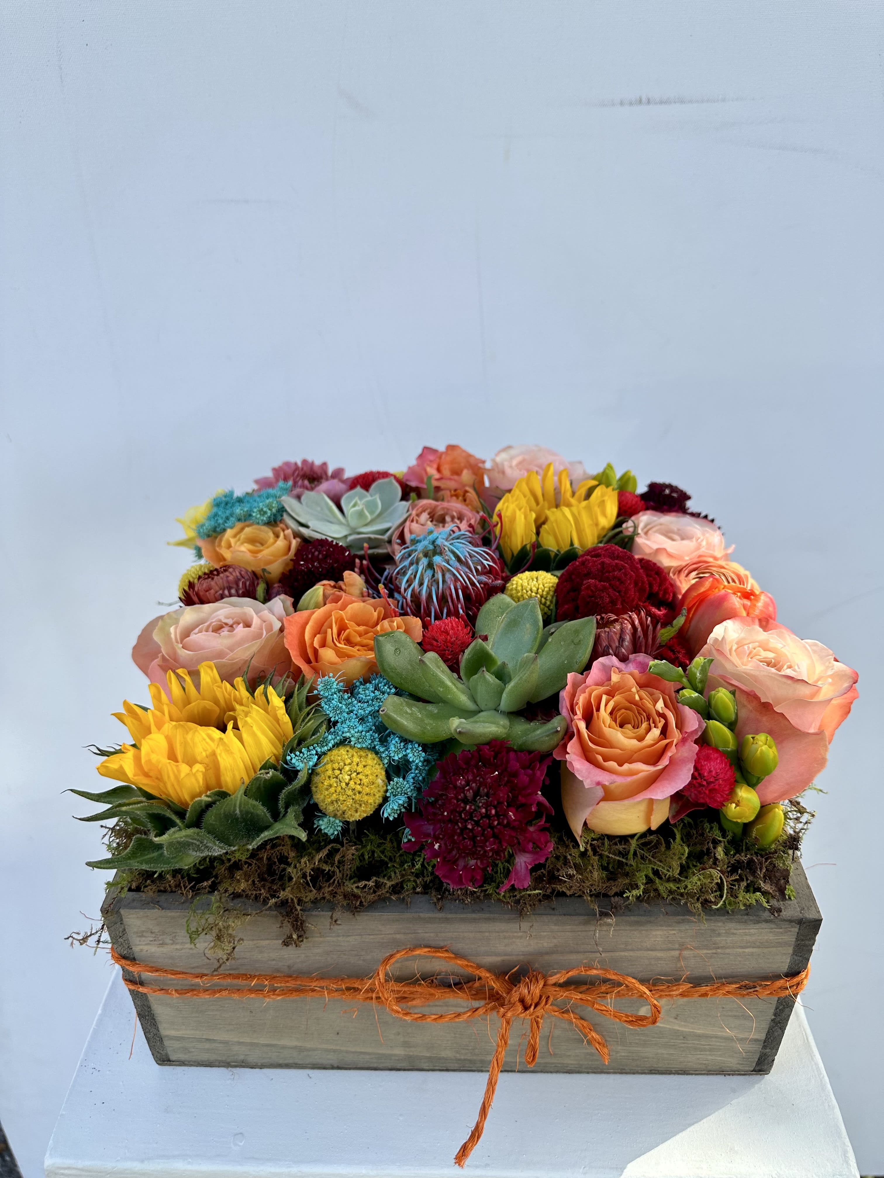 Colorful mixed flower arrangement in a wooden box with an orange ribbon
