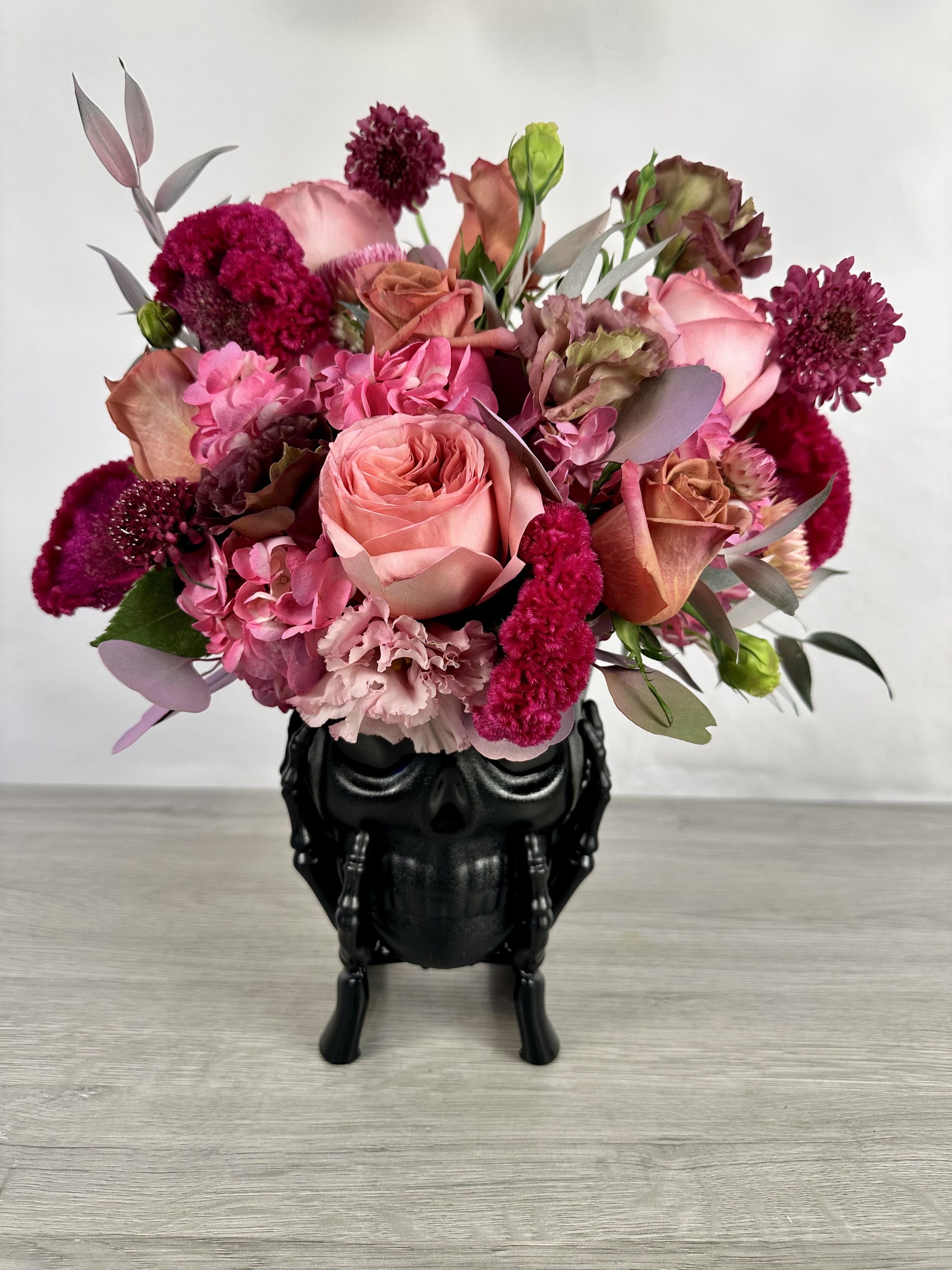 Pink and burgundy bouquet in a black skull vase