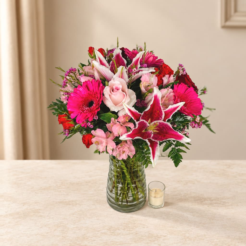 Pink and red mixed bouquet in a glass vase with a small candle beside it