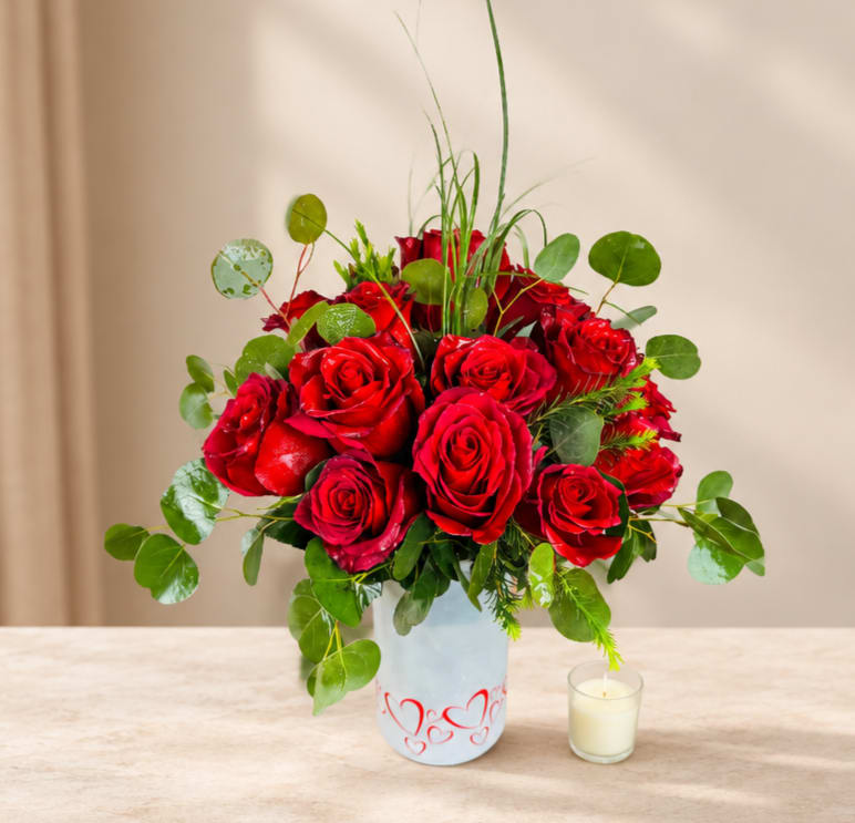 Red roses arranged in a white vase with a small candle beside it