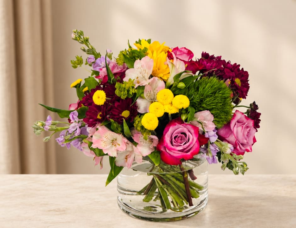 Mixed bouquet of roses, daisies, and alstroemeria in a clear glass vase