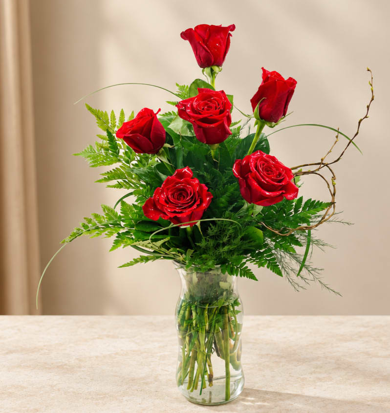 Red roses arranged in a clear glass vase with green foliage
