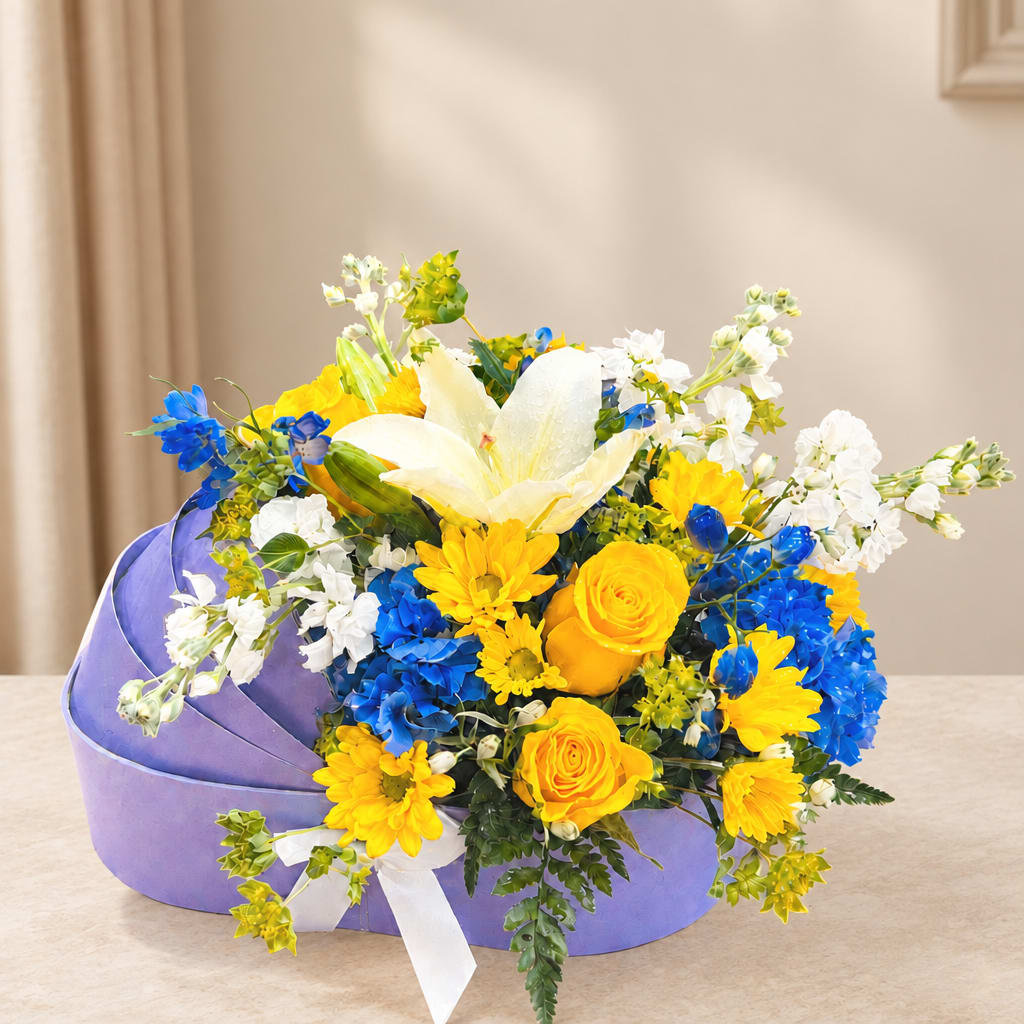 Yellow and blue mixed flower arrangement in a purple box with a white ribbon