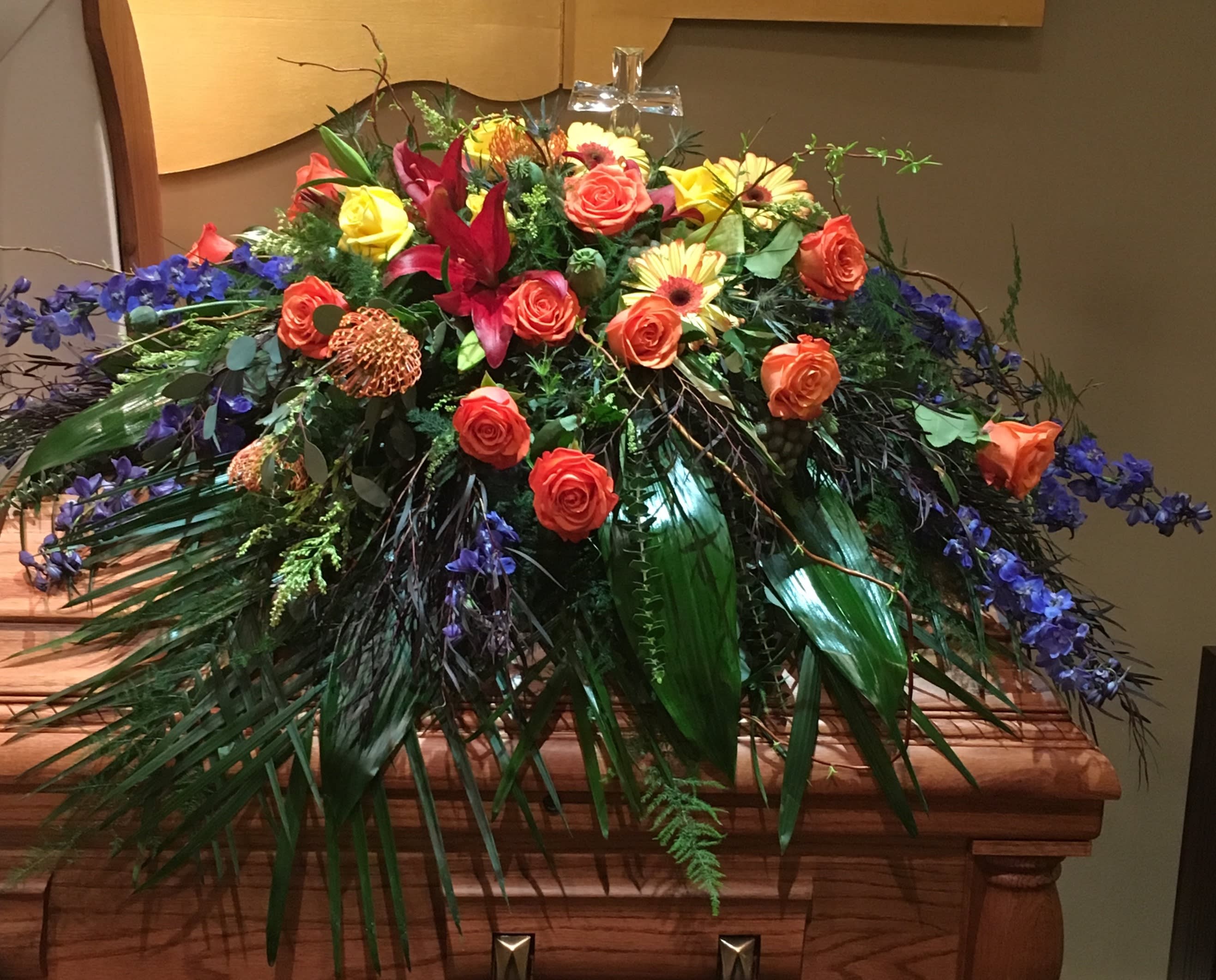 Large casket spray with orange and yellow roses and purple flowers