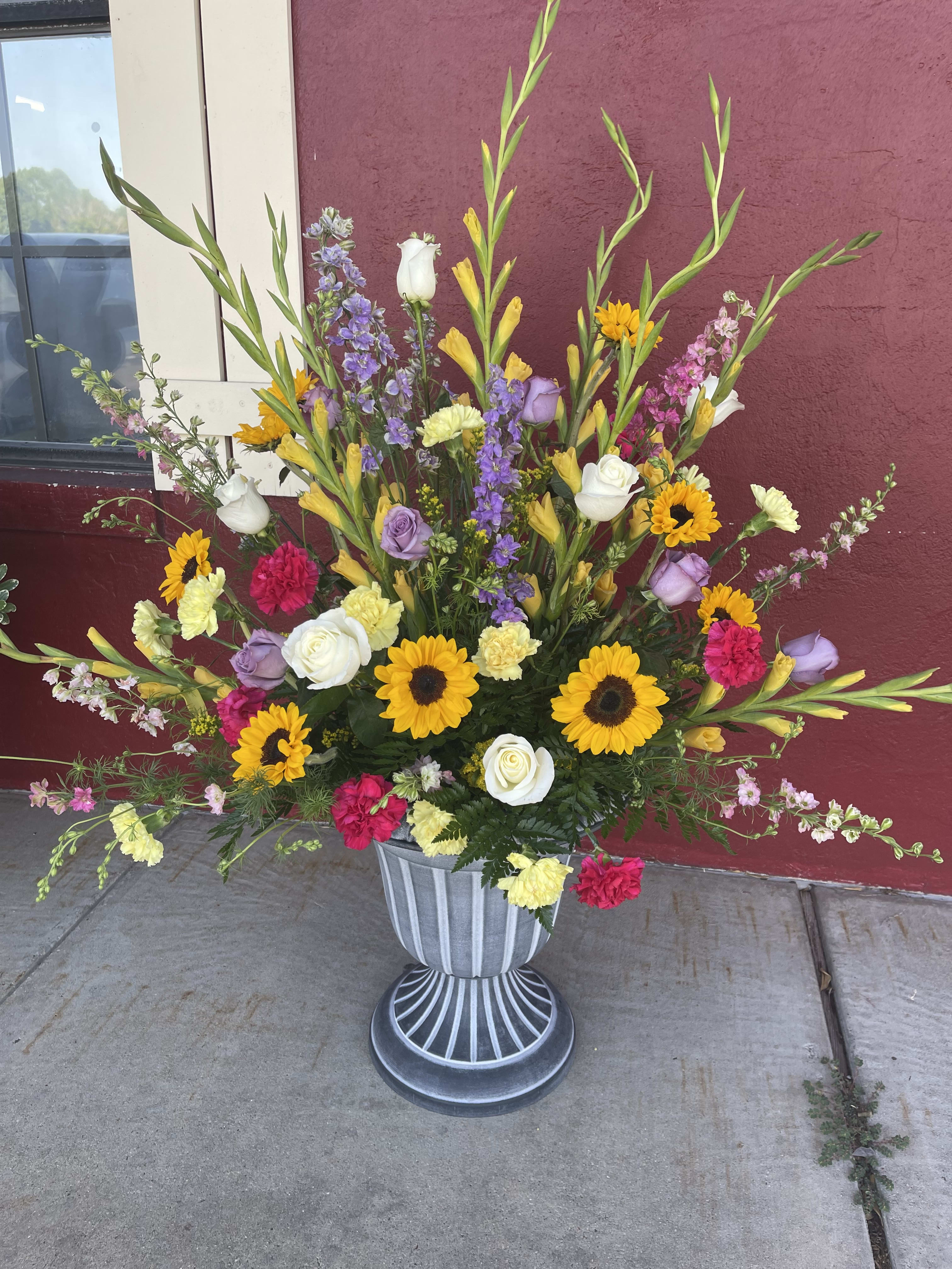 Tall mixed flower arrangement in a gray urn with sunflowers and roses