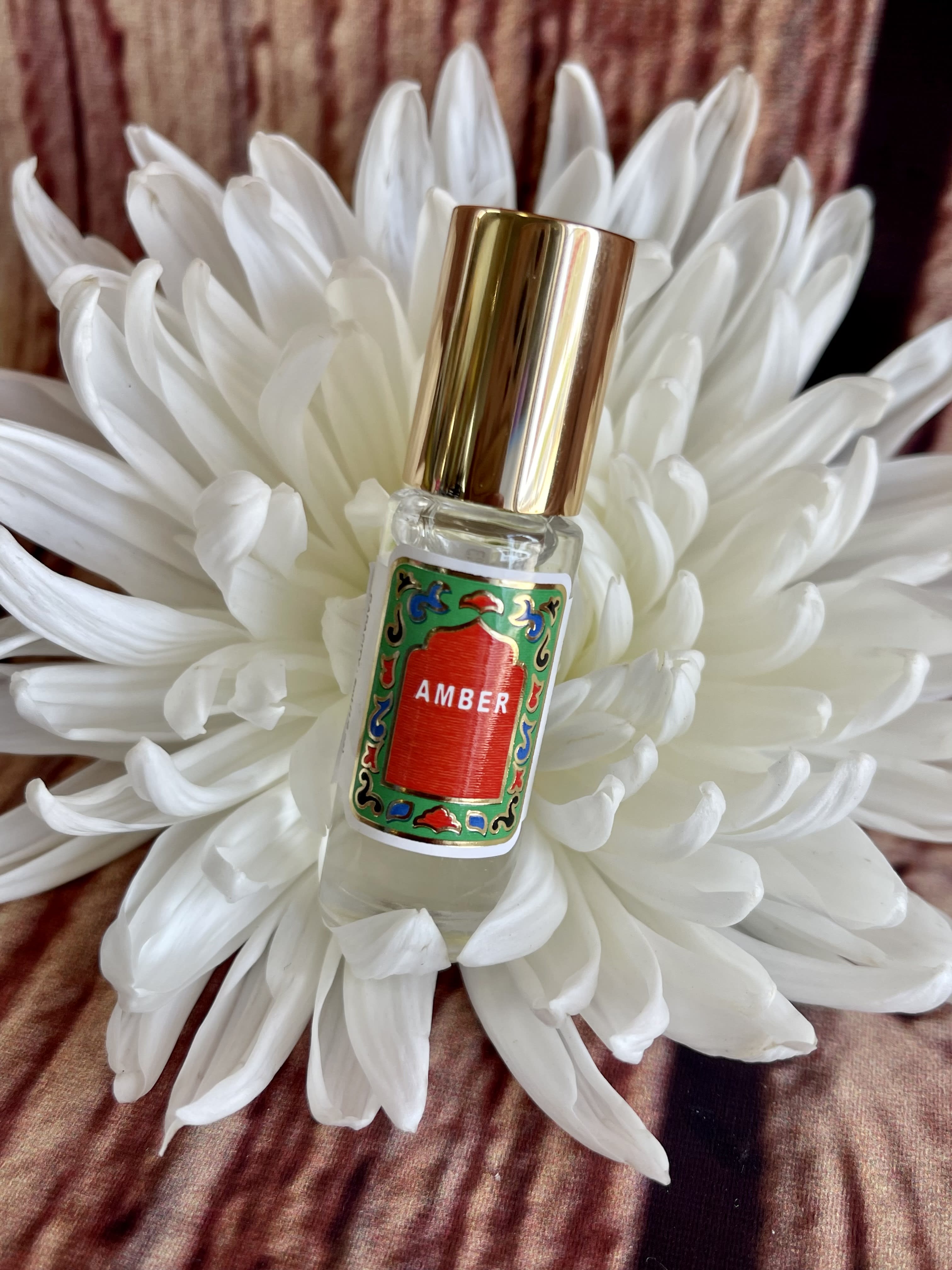 White flower with a small perfume bottle labeled Amber in the center