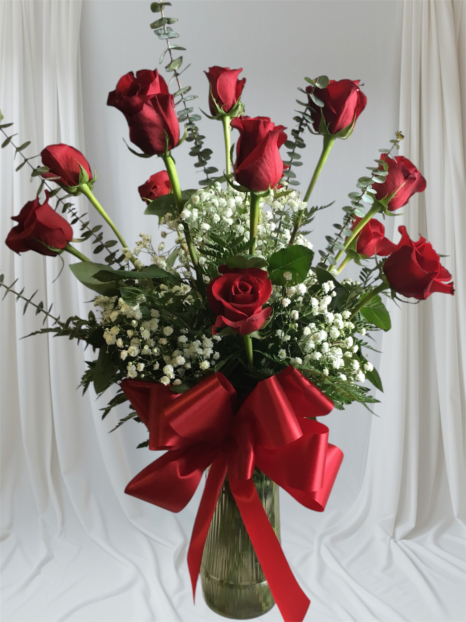 Tall bouquet of red roses with baby's breath in a glass vase and red ribbon
