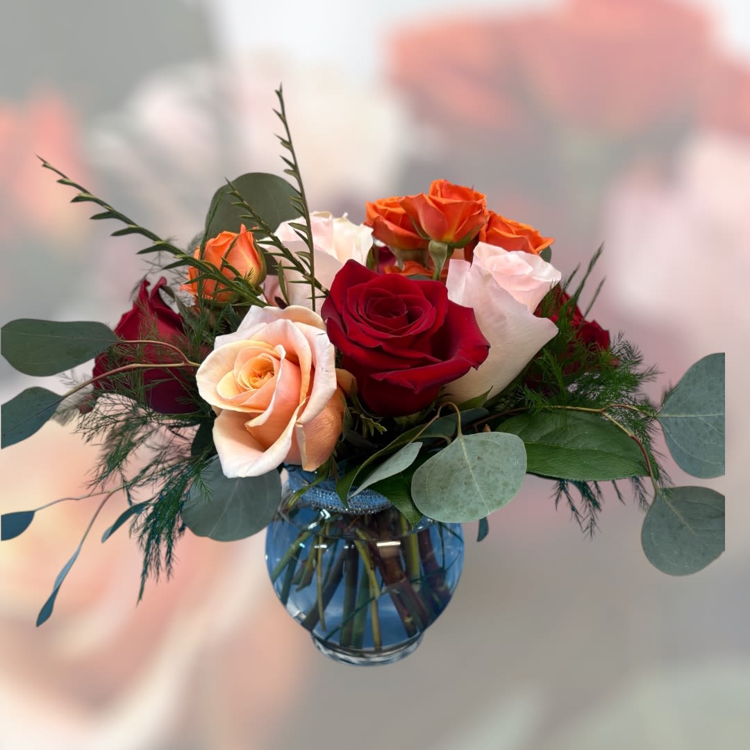 Bouquet of red, peach, white, and orange roses in a blue glass vase