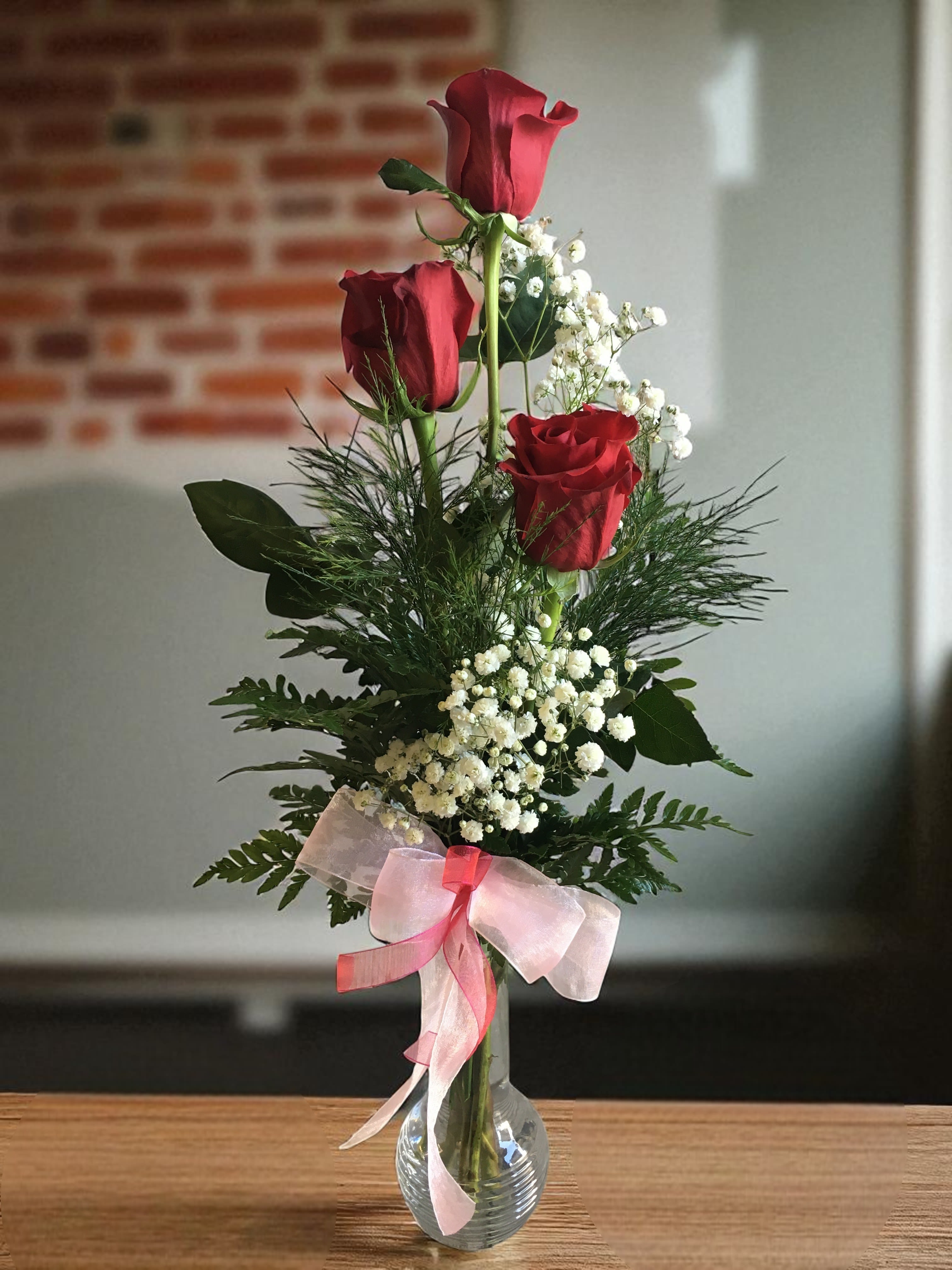 Tall vase arrangement with red roses, baby's breath, and a pink ribbon