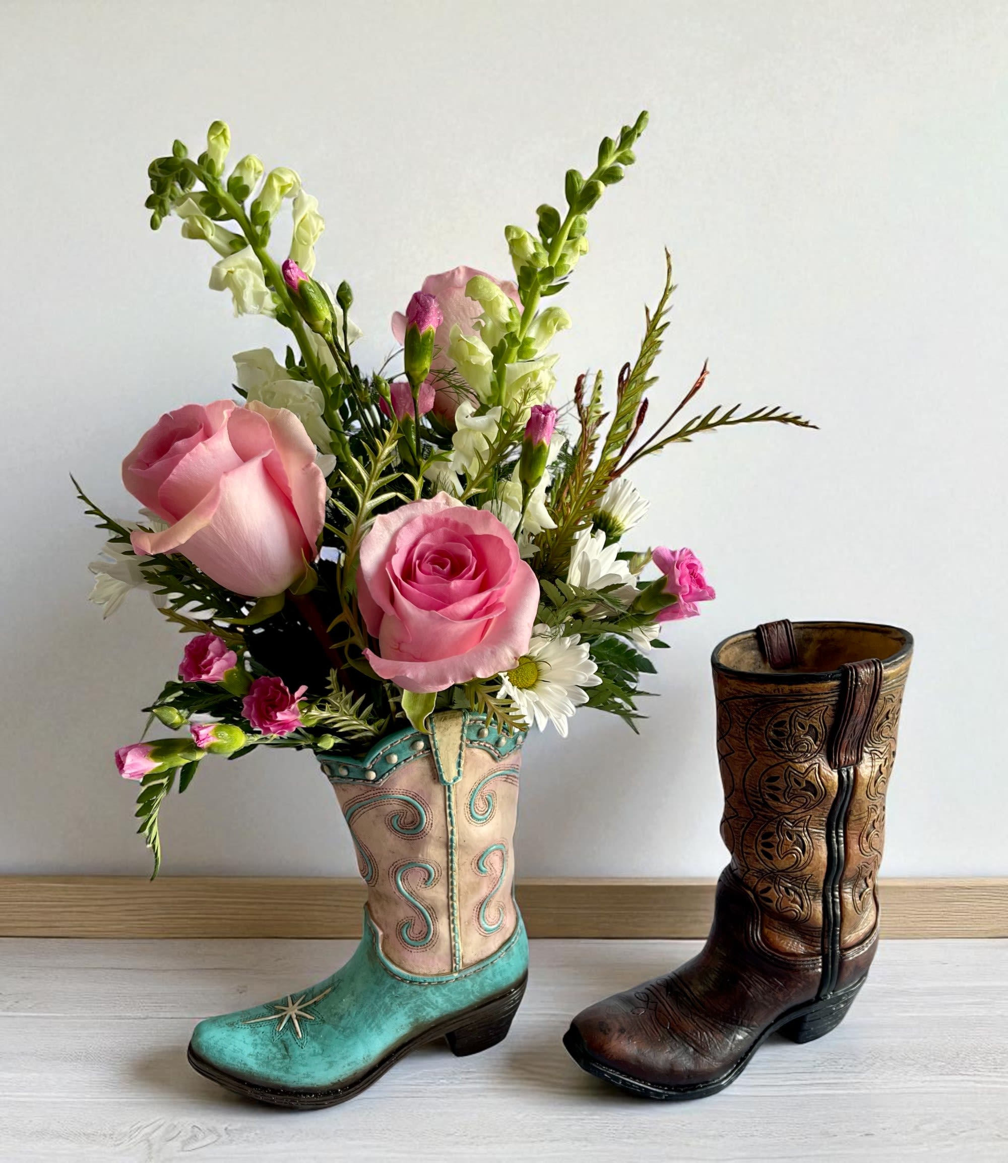 Pink rose bouquet arranged in a turquoise cowboy boot vase beside a brown boot