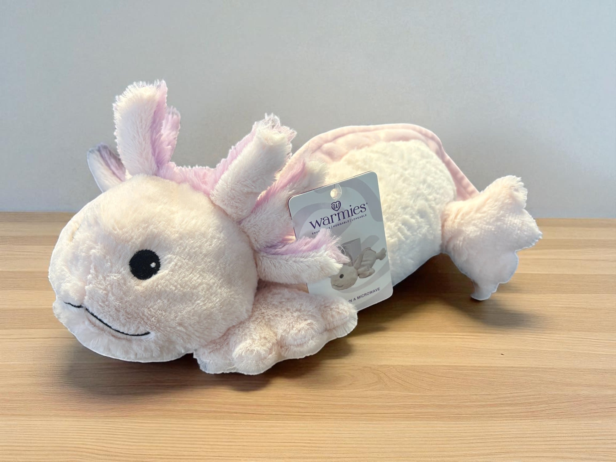 Plush pink-and-white axolotl toy with a product tag