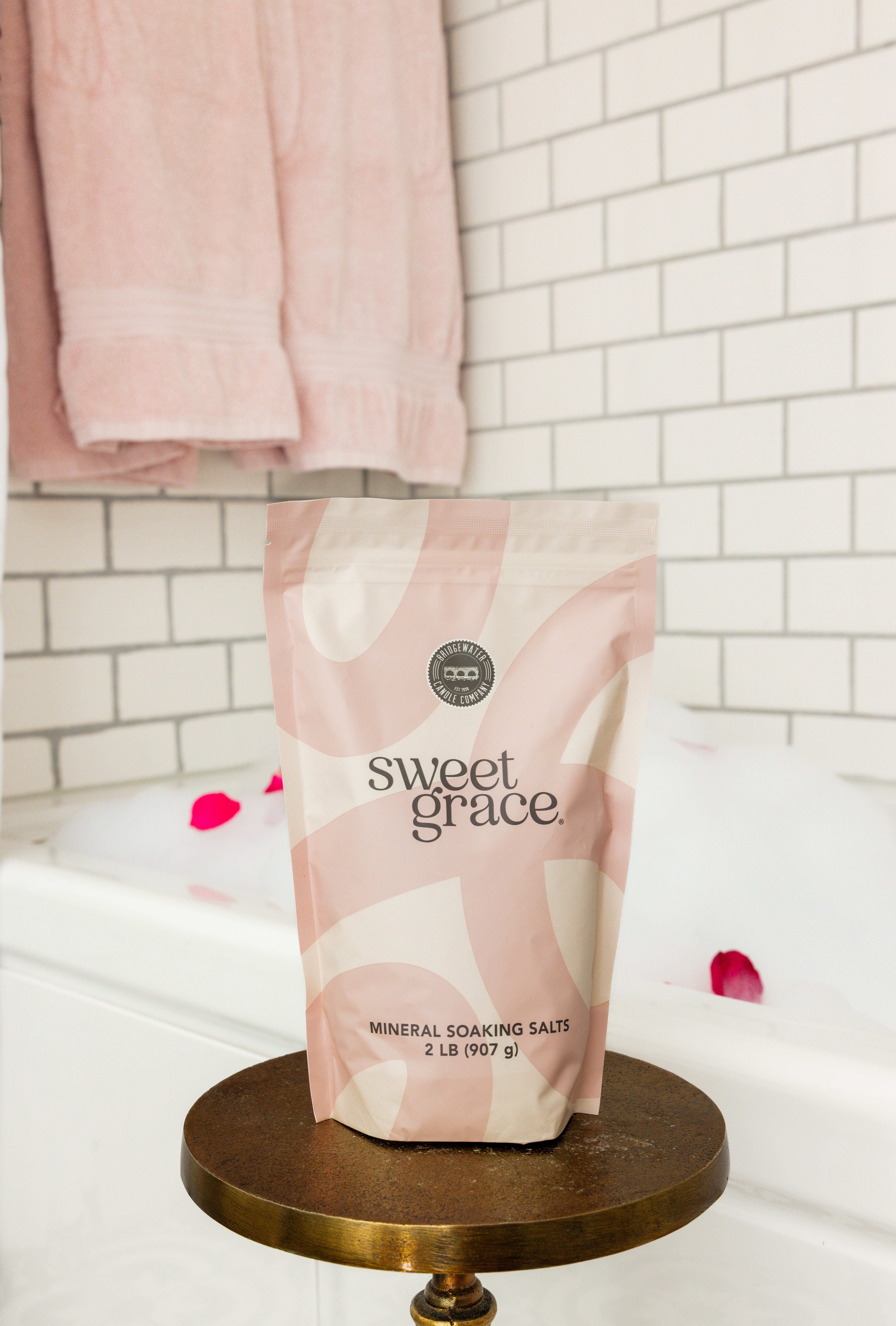 A pink and cream pouch of mineral soaking salts on a round stand.