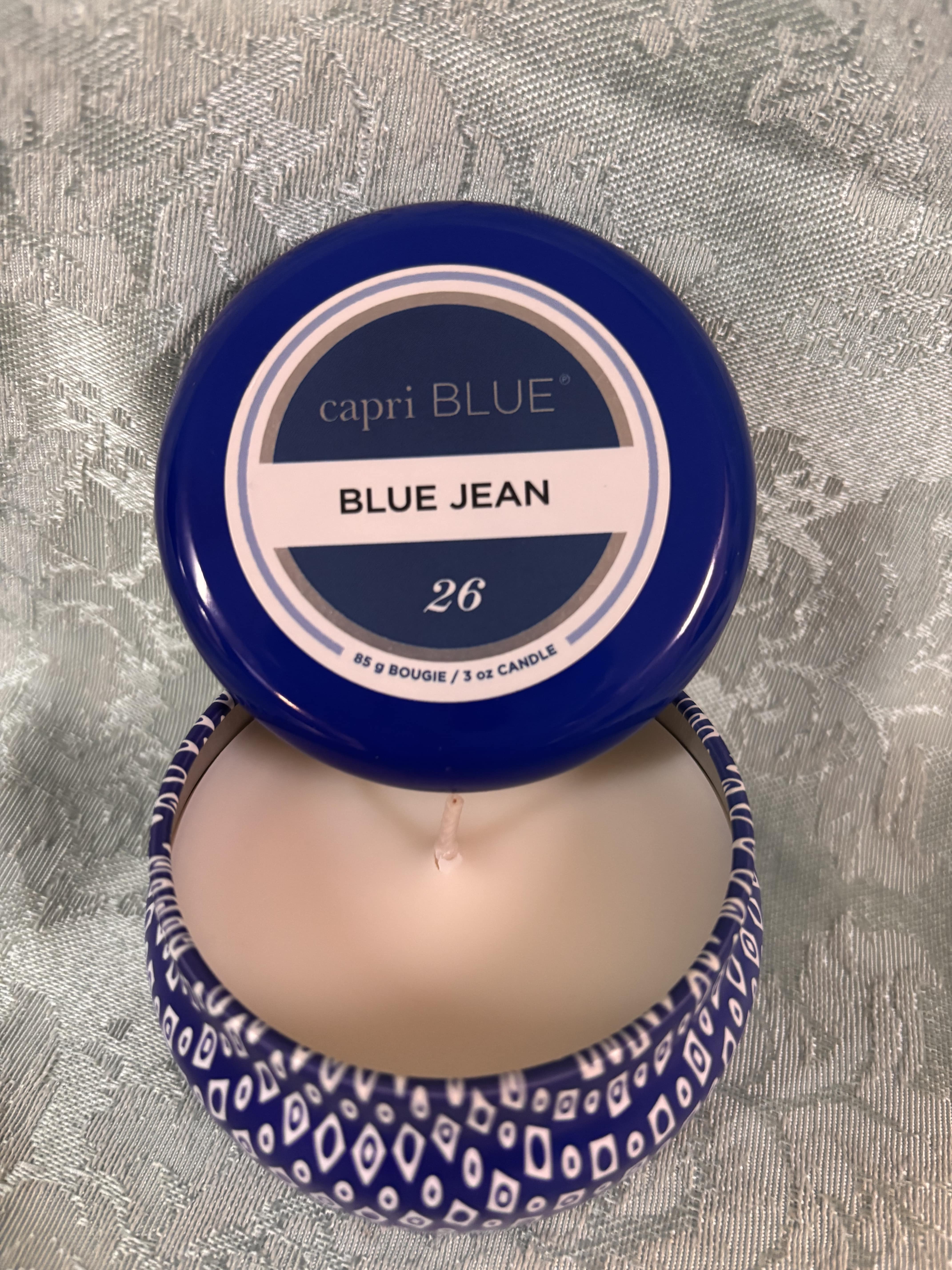Blue-lidded candle tin labeled Blue Jean, shown open with a pale wax candle inside.