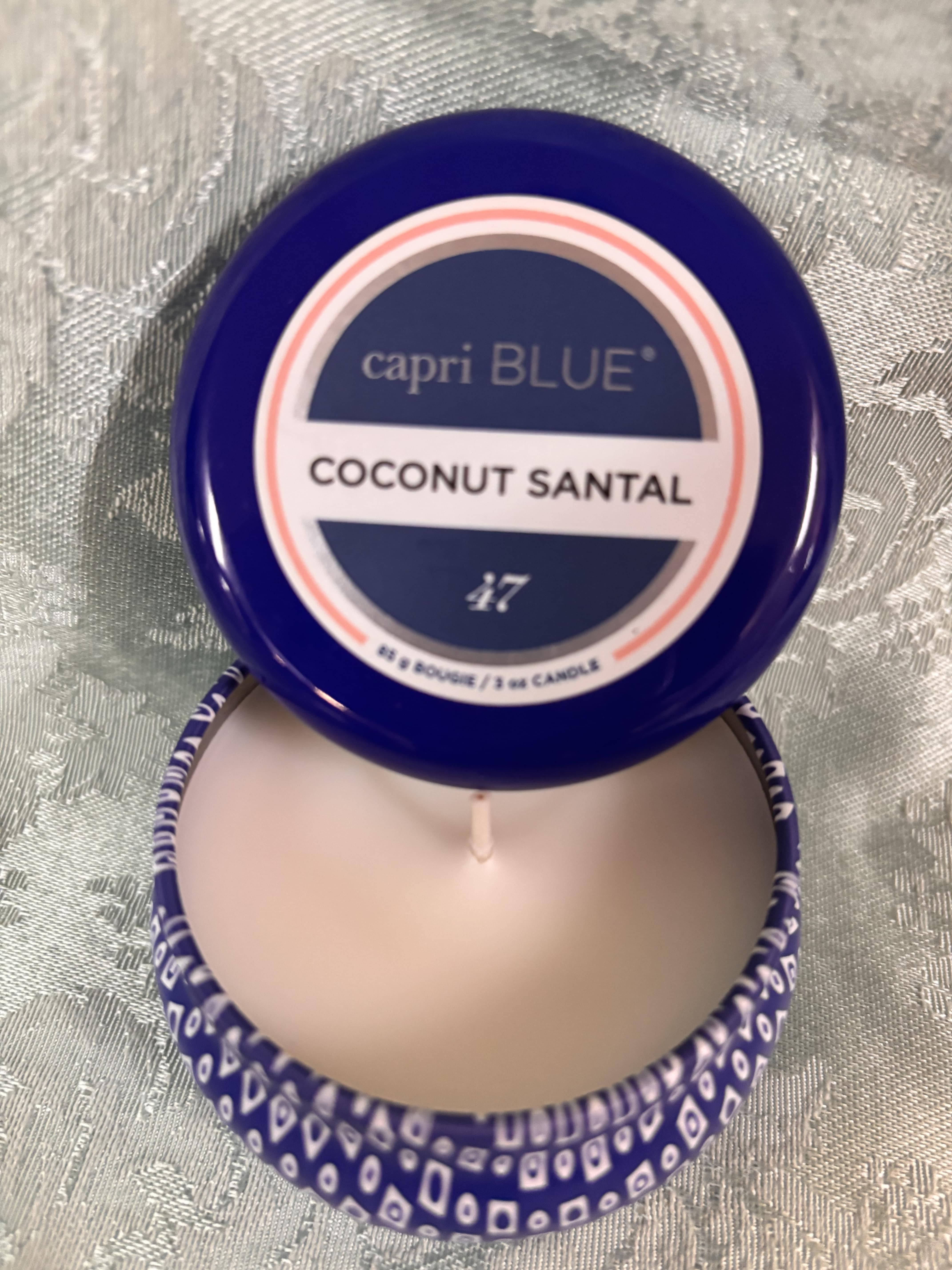 Blue-lidded candle tin labeled Coconut Santal on a patterned surface