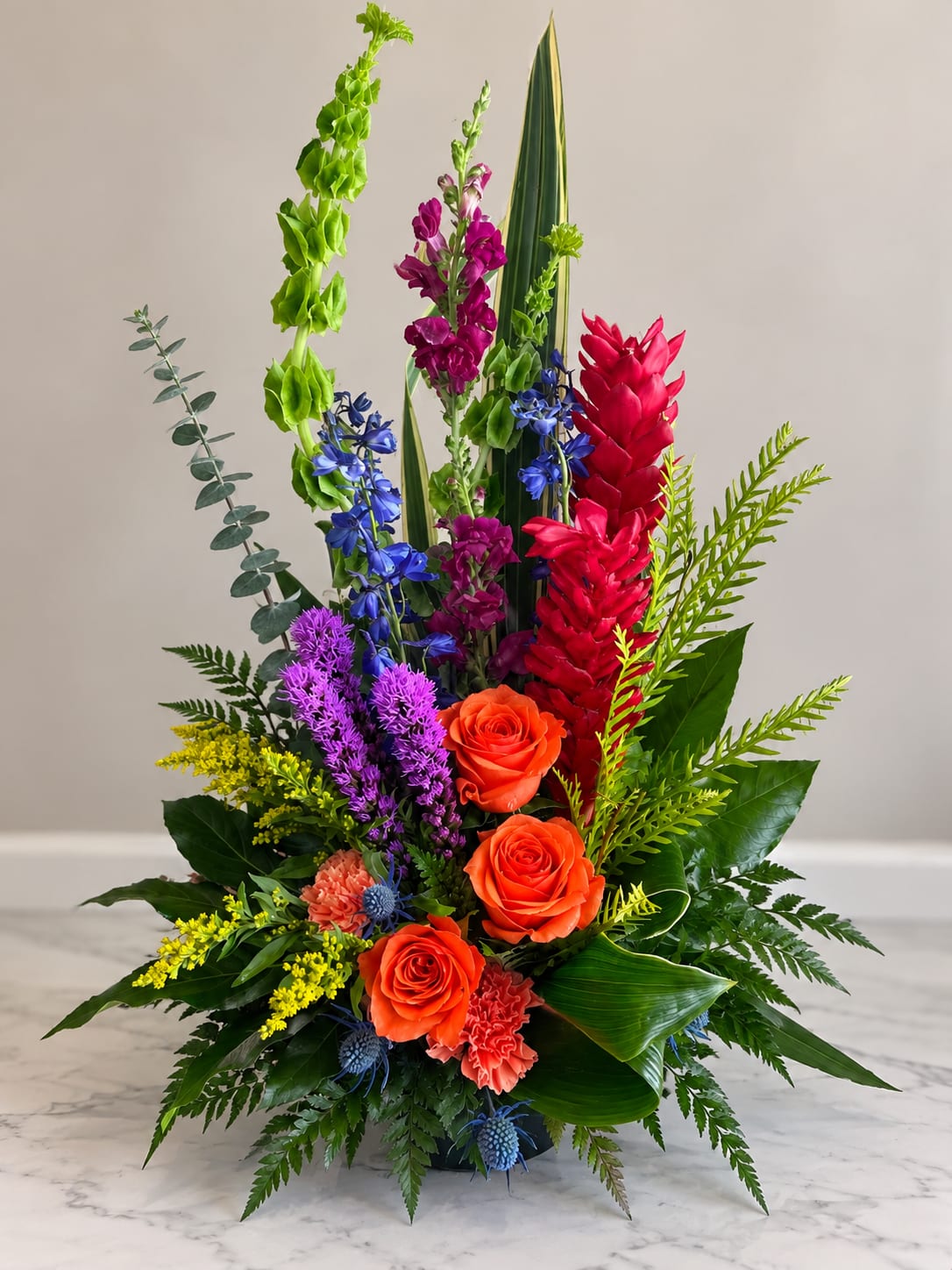 Tall multicolor floral arrangement with orange roses and bright tropical blooms
