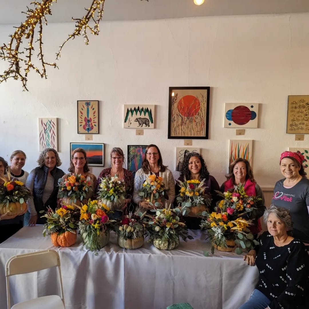 Group of women holding colorful floral arrangements in a gallery room
