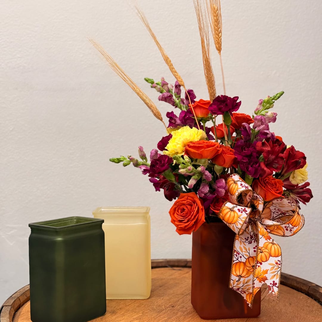 Orange and purple flower arrangement in a brown vase with a pumpkin ribbon