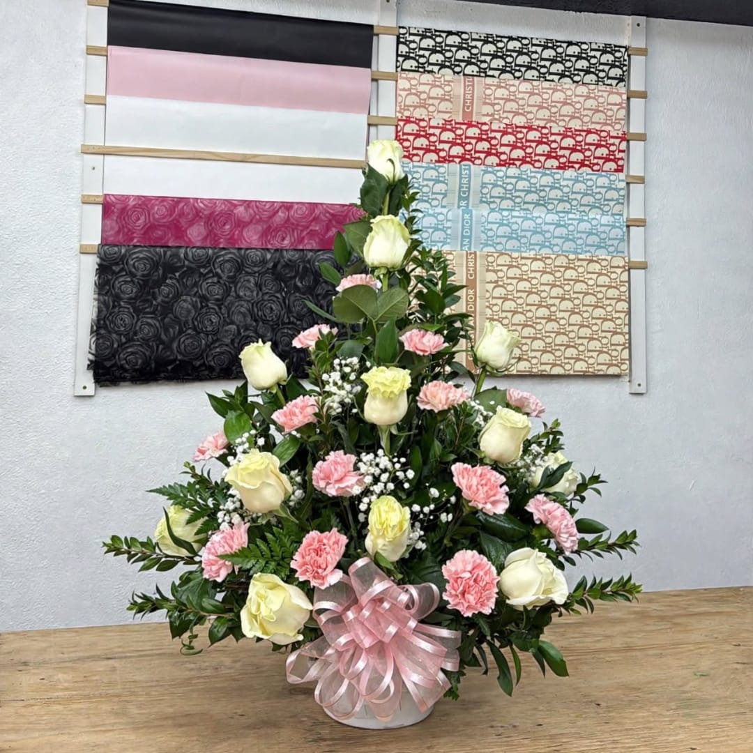Pink and cream rose arrangement with carnations in a white vase and pink ribbon