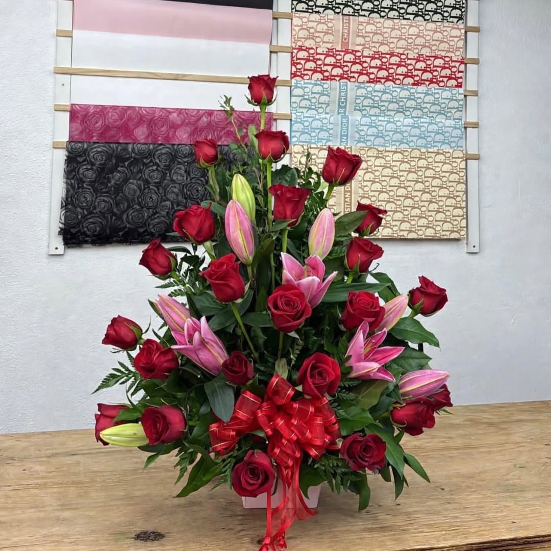 Red roses and pink lilies in a white vase with a red bow