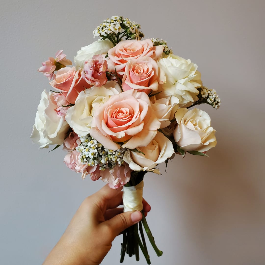 Handheld bouquet of peach and white roses with small white filler flowers