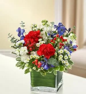 In my Thoughts - Red, White and Blue - Product ID: 95442  This lovely red, white and blue sympathy arrangement offers a beautiful reflection of your patriotism, sympathy and support. Fresh red roses, delphinium, stock, carnations and hypericum, designed in a cube vase, provide a stunning tribute sent to the home or service. Elegant red, white and blue arrangement of roses, delphinium, stock, carnations, hypericum and monte casino, accented with variegated pittosporum and spiral eucalyptus Artistically designed by our florists in a classic clear glass cube vase lined with a Ti leaf ribbon; vase measures 5"H x 5"D Appropriate for the service or for sending to the home or office of friends and family members to honor a military veteran Large arrangement measures approximately 11"H x 11"L Medium arrangement measures approximately 10"H x 10"L Small arrangement does not include roses and measures approximately 9"H x 9"L Our florists hand-design each arrangement, so colors, varieties, and container may vary due to local availability