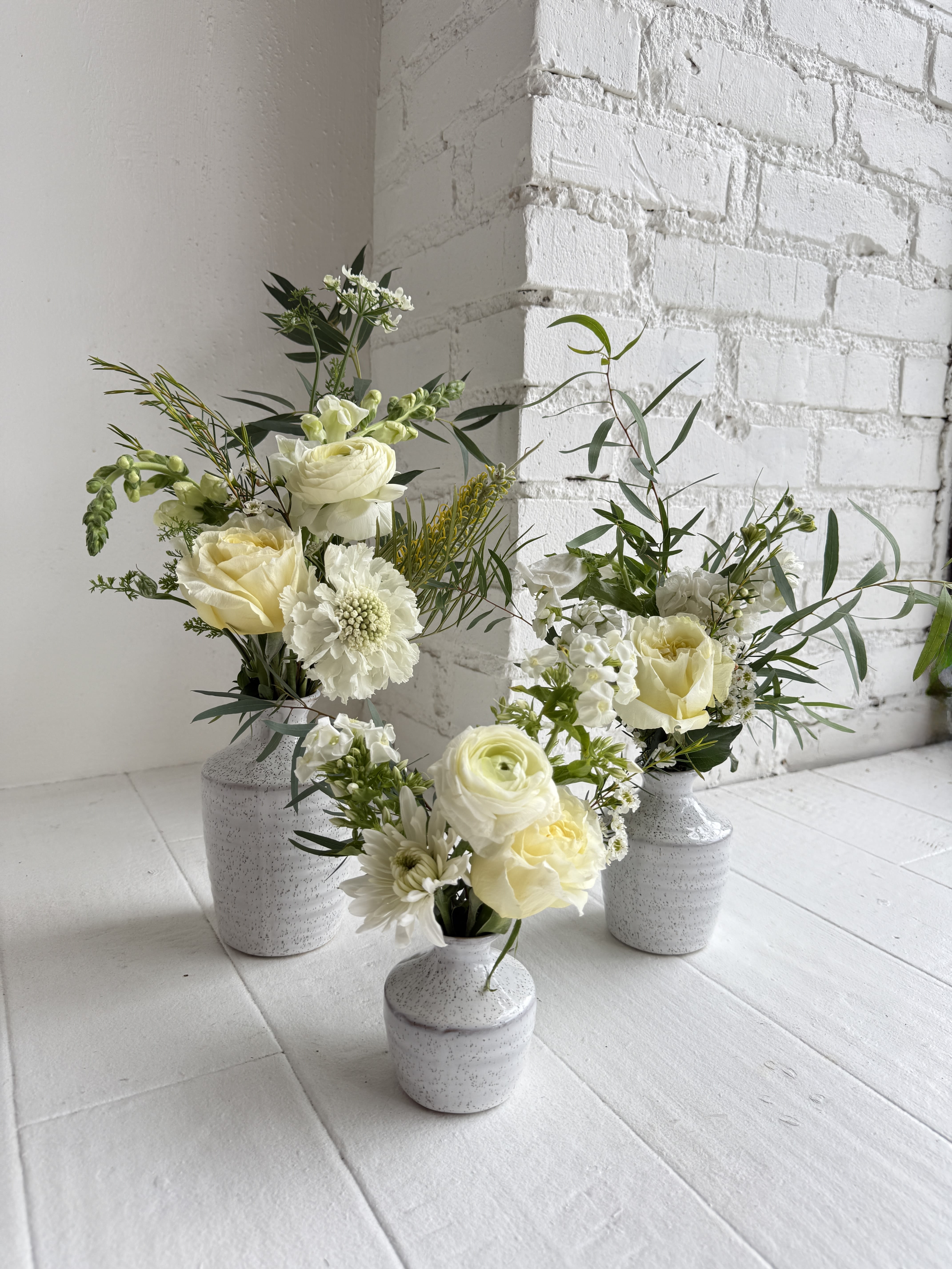 Simone - An eclectic mix of seasonal white flowers with foliage in a set of three vases. 